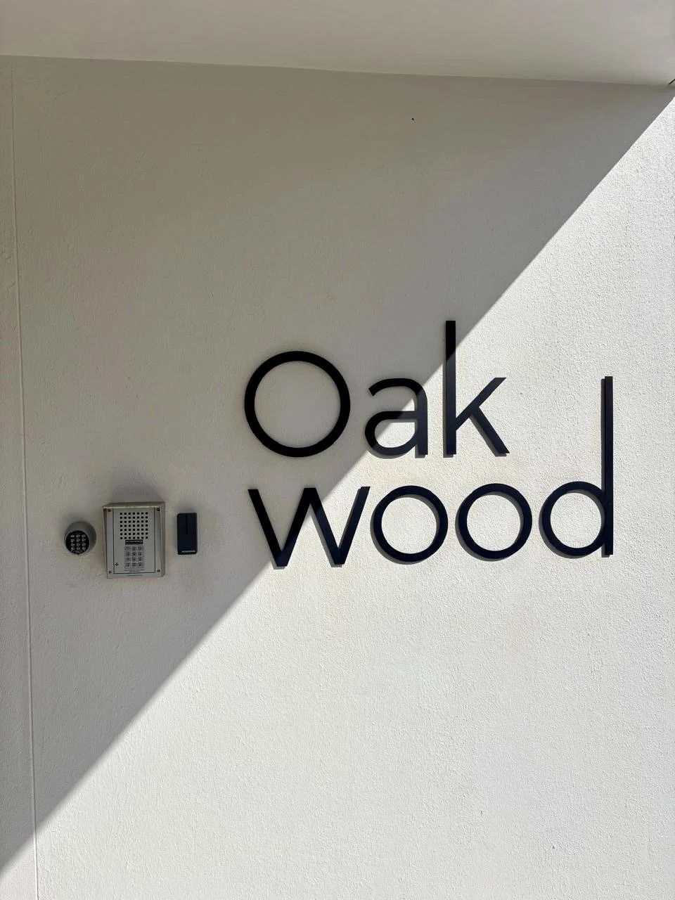 The image shows a wall with a sign that reads 'oak wood' and an electronic access panel below it. The wall is split into a shadowed and a lit area.