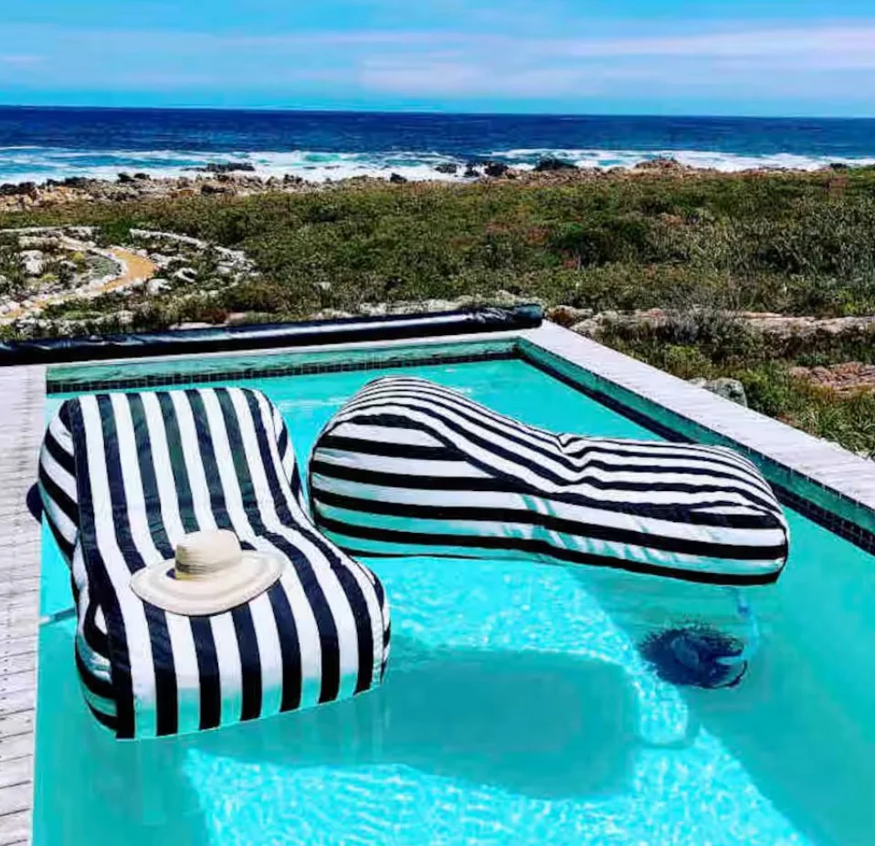 A swimming pool with striped lounge chairs and a beach view in the background.