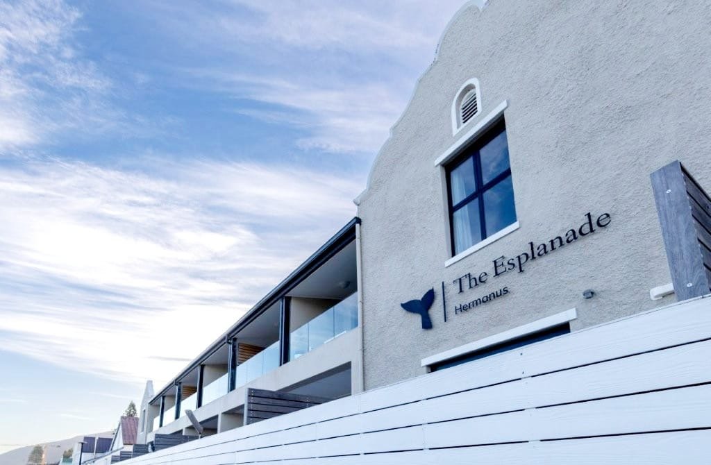 Exterior of a modern building with the sign 'The Esplanade Hemnans' and a whale tail logo, featuring balconies and a cloudy sky.