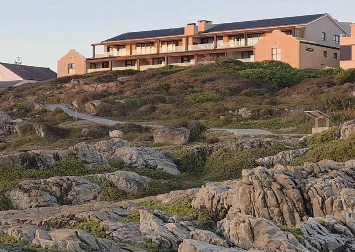 A large house located on a rocky hill with a winding path leading to it, surrounded by greenery and rocks.