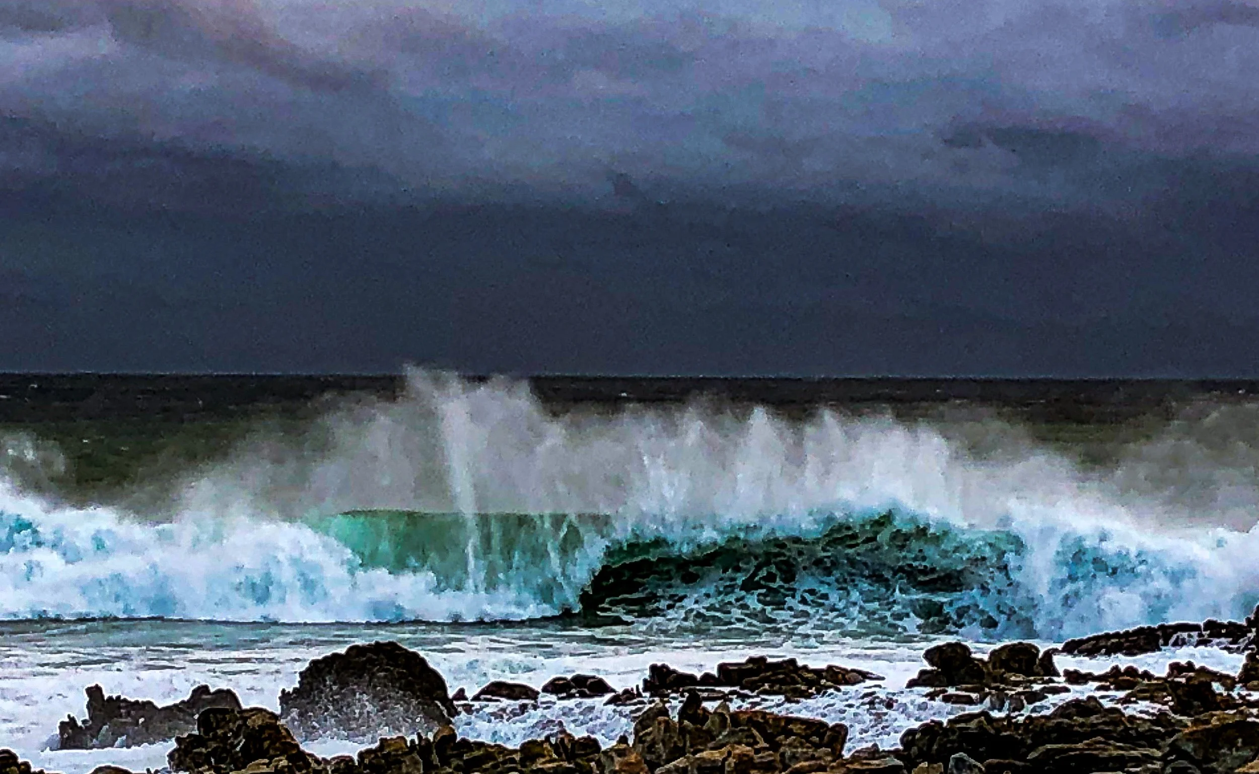 Waves crashing on a rocky shoreline under a cloudy, dark sky.