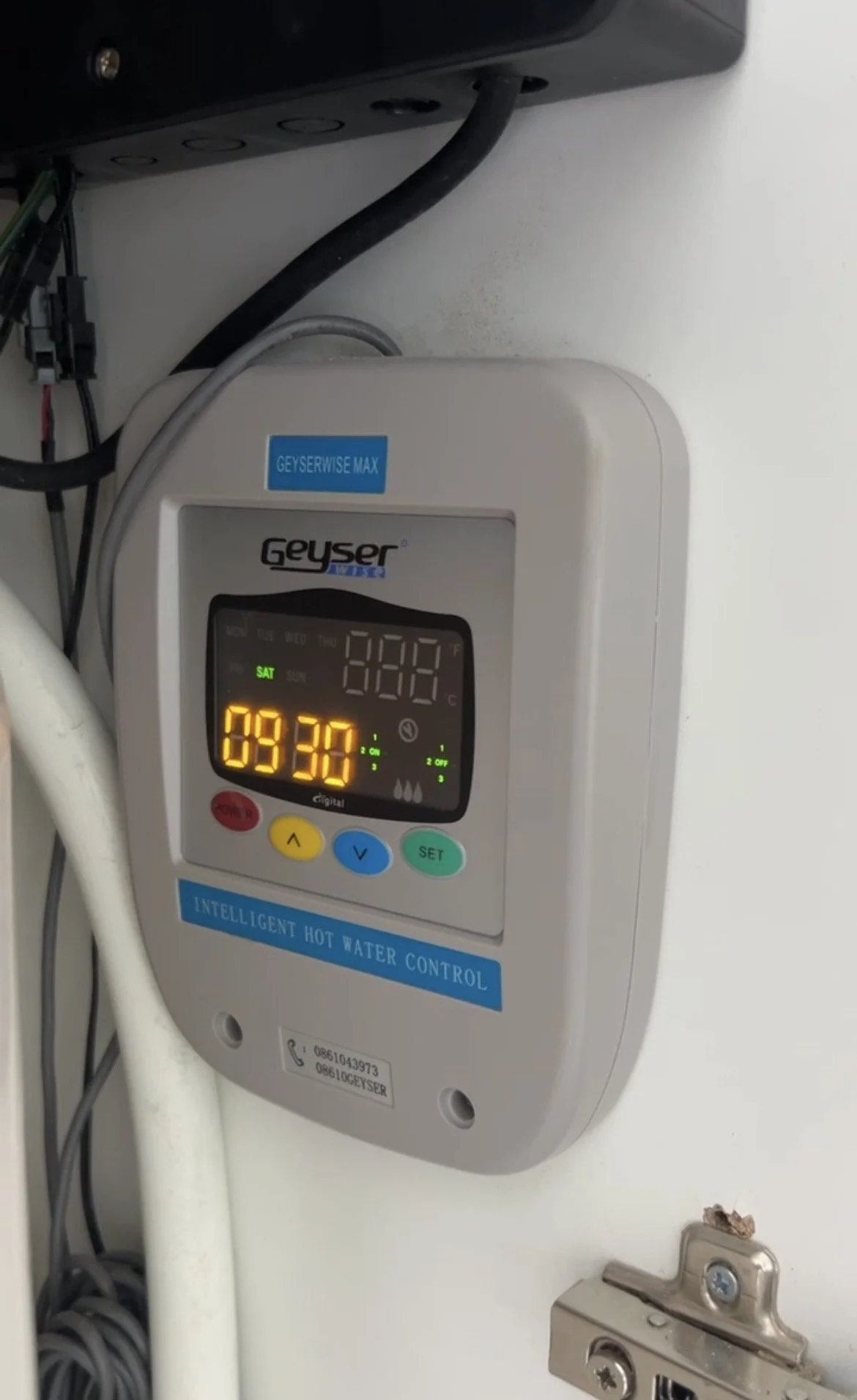 A digital smart water heater control panel mounted on a wall with blue and green buttons, showing the time as 09:30.