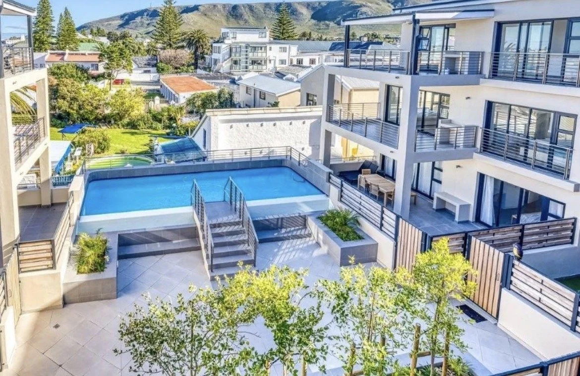 A modern multi-story apartment complex with balconies, outdoor swimming pool, and surrounding greenery in a mountainous area.