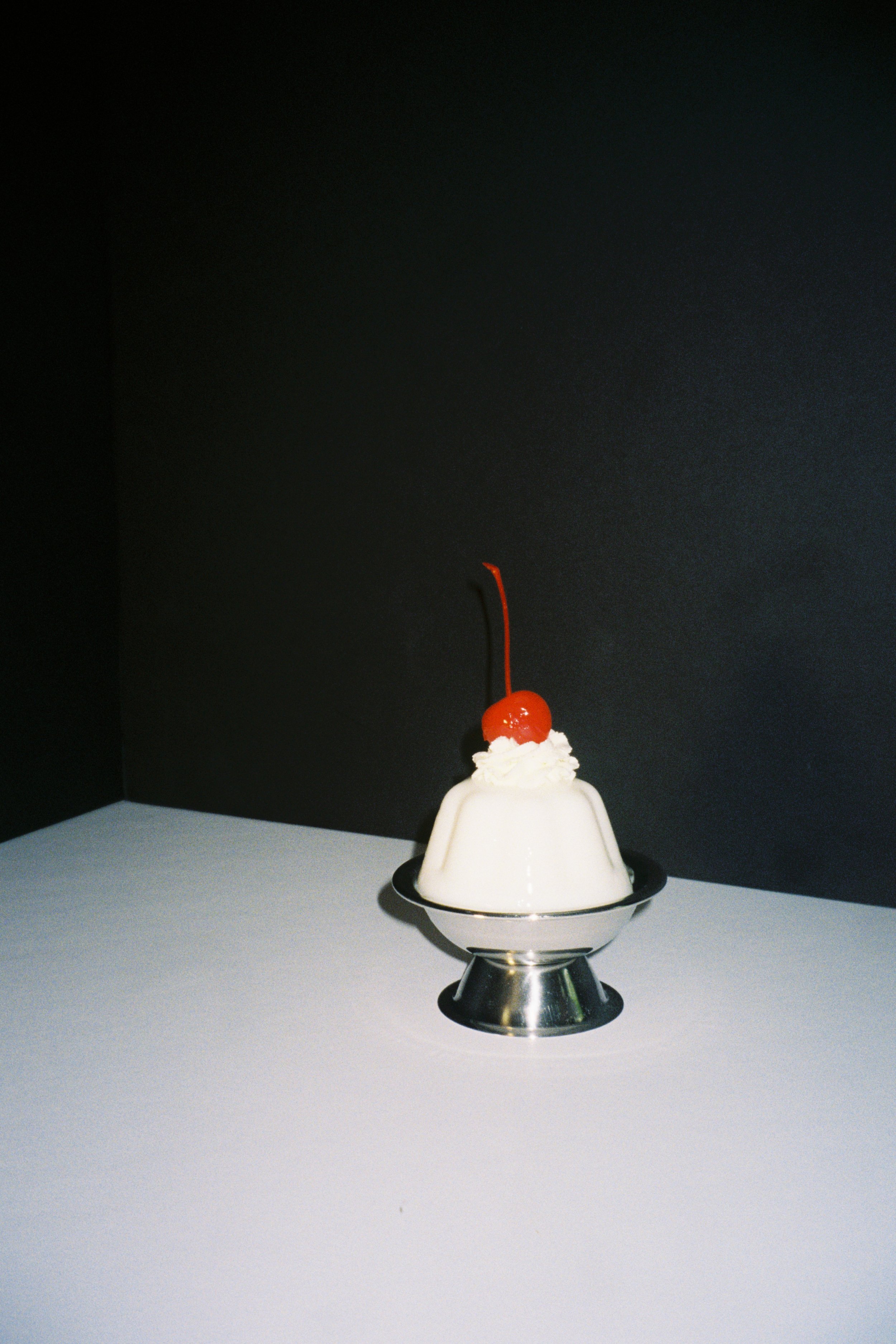 A vintage-style sundae with whipped cream and a cherry on top, served in a metallic dish against a black and white background.