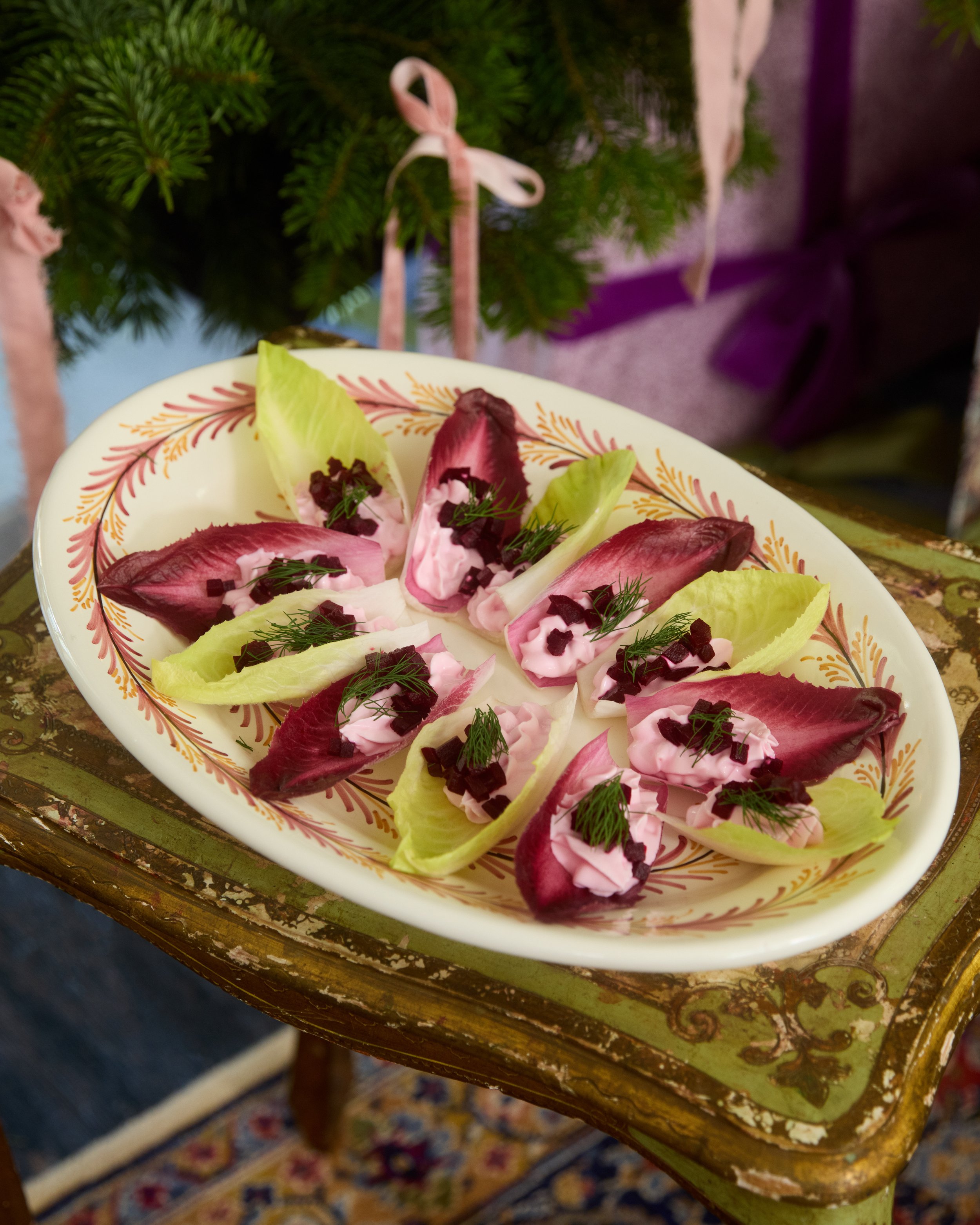 Fresh salad with endive leaves, pink cream cheese, chopped black olives, and garnished with dill, served on a decorative plate.