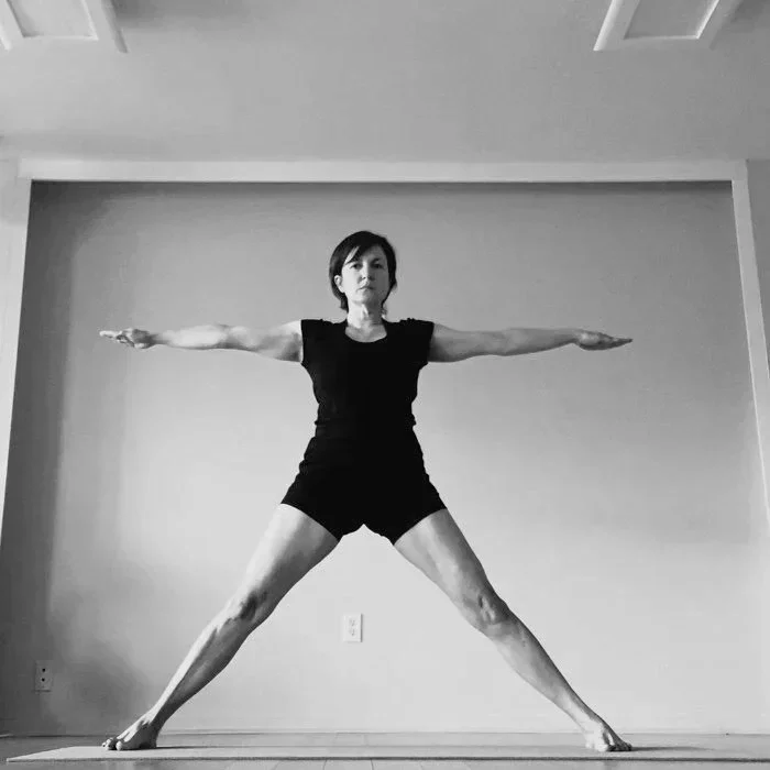 Woman practicing yoga or stretching in a living room, standing with legs apart and arms outstretched
