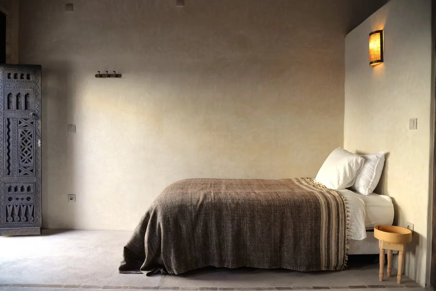 Minimalist bedroom with bed, pillows, bedside table, wall-mounted lamp, and textured wall decor.
