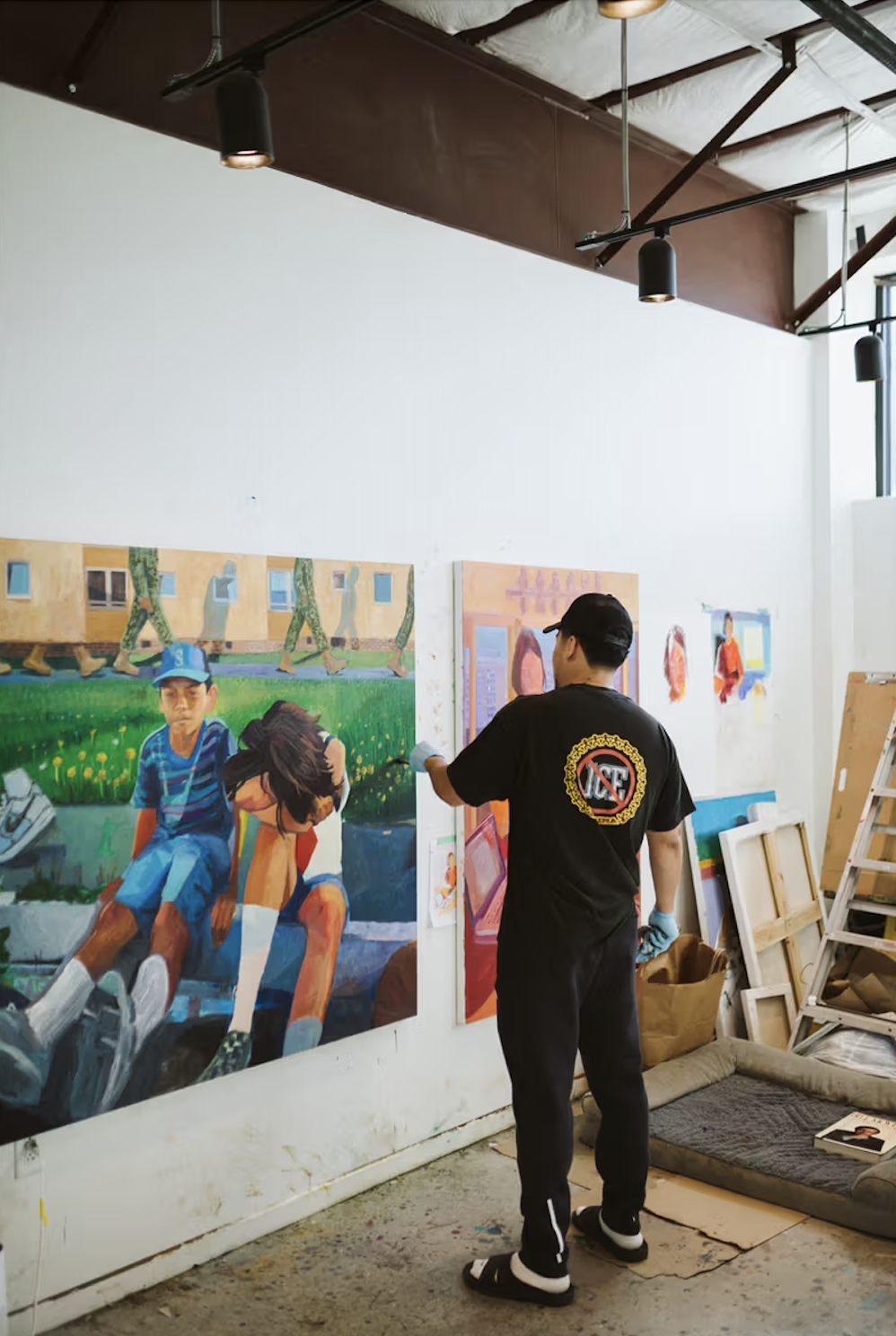 An artist working on a colorful mural in an art studio with various paintings and art supplies around.
