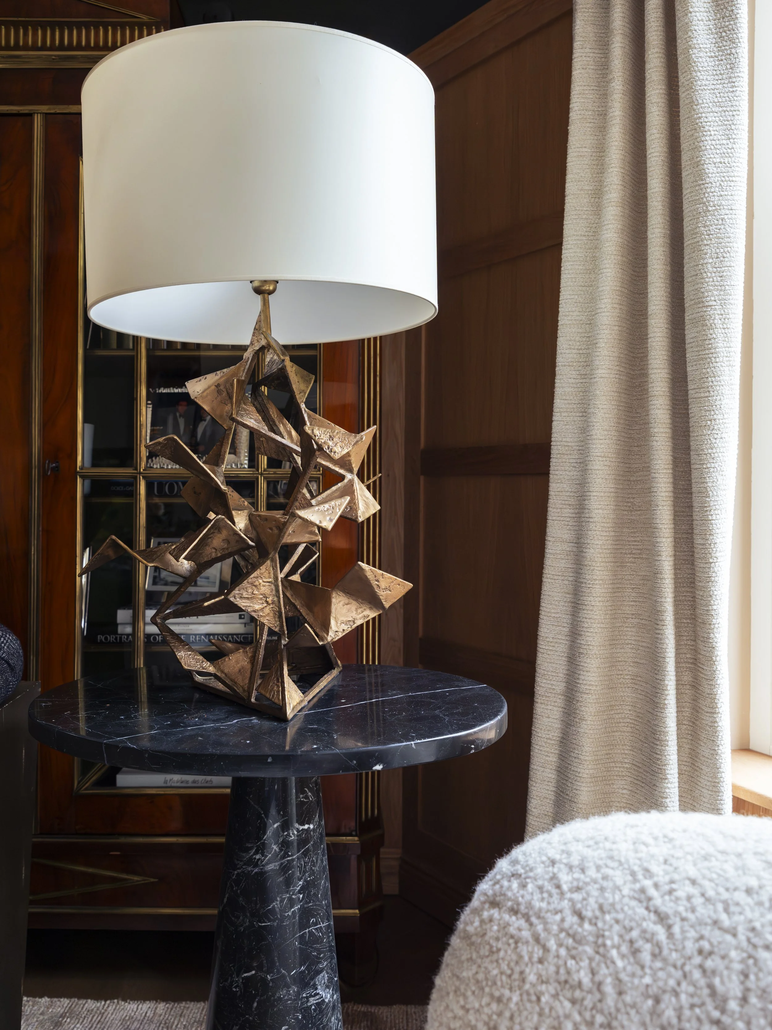 Decorative table lamp with an abstract bronze-colored base and a white lampshade on a black marble side table in a living room.