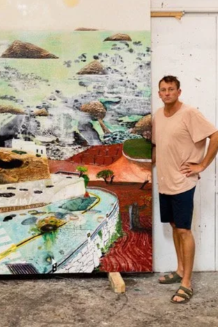 Man standing next to a colorful mural featuring a landscape with rocks, water, and greenery.