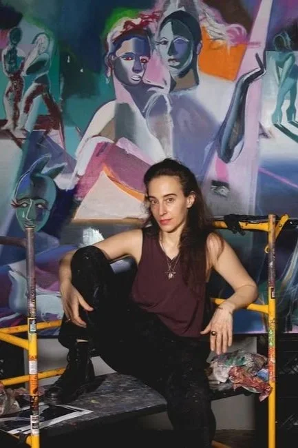 An artist sitting in front of a colorful abstract mural, with artistic tools and scaffolding around her.