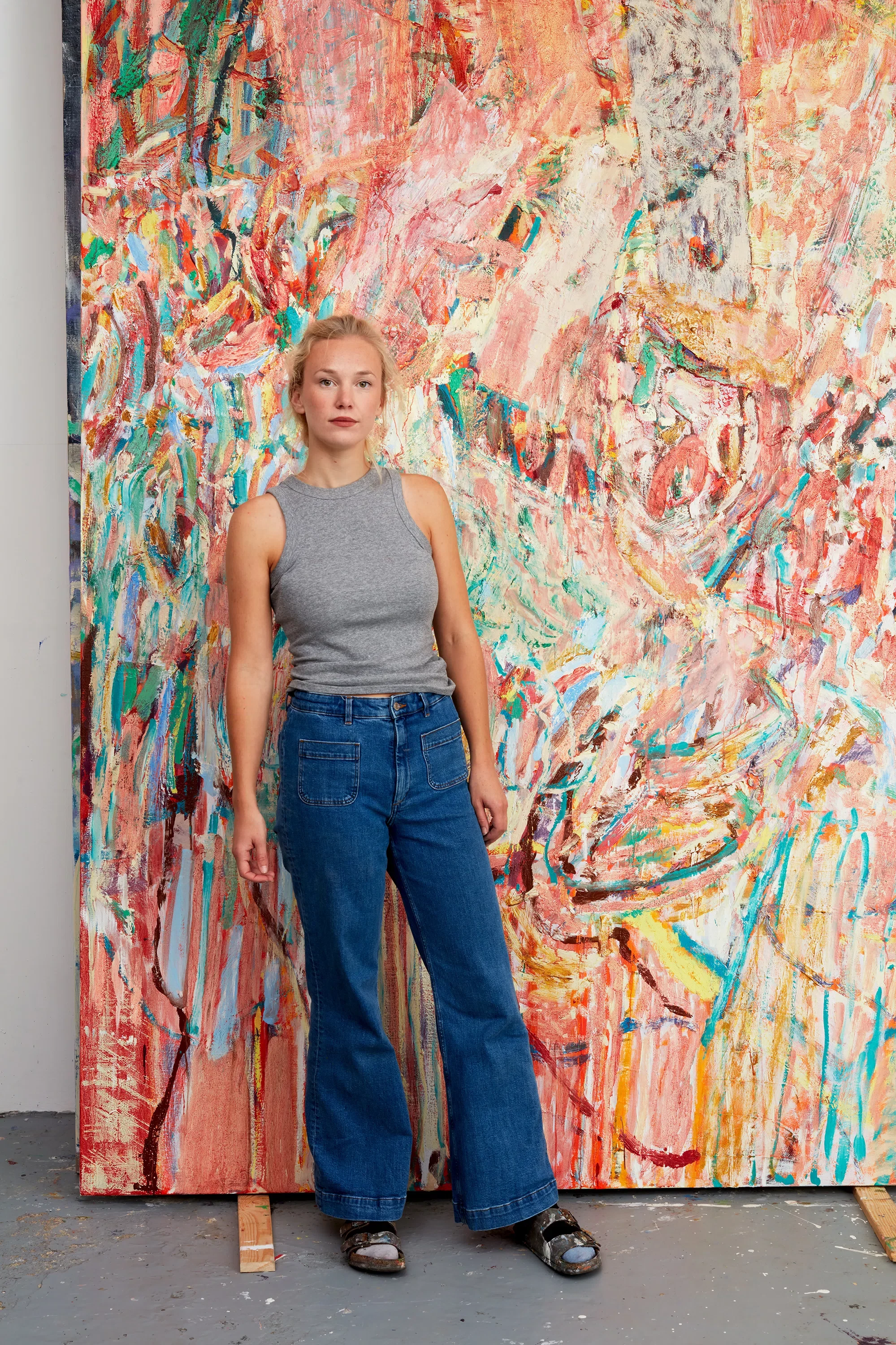 A woman standing in front of a large abstract painting with swirling and colorful brushstrokes.