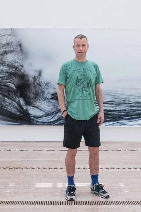 Man standing in front of an abstract black and white artwork at an art gallery or museum.