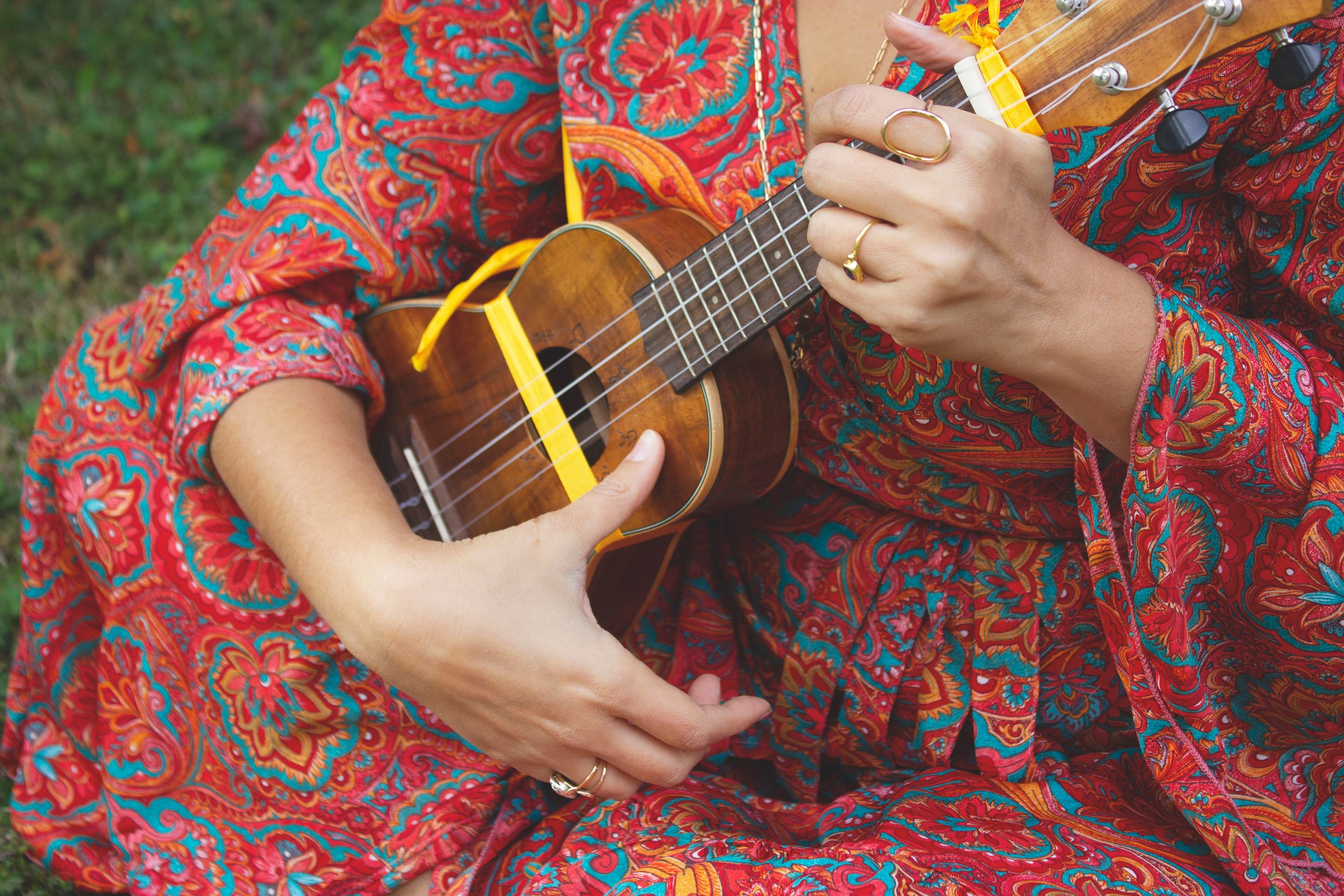Una persona che indossa un abito colorato con motivo floreale arancione, rosso e blu mentre suona una chitarra acustica all'aperto.