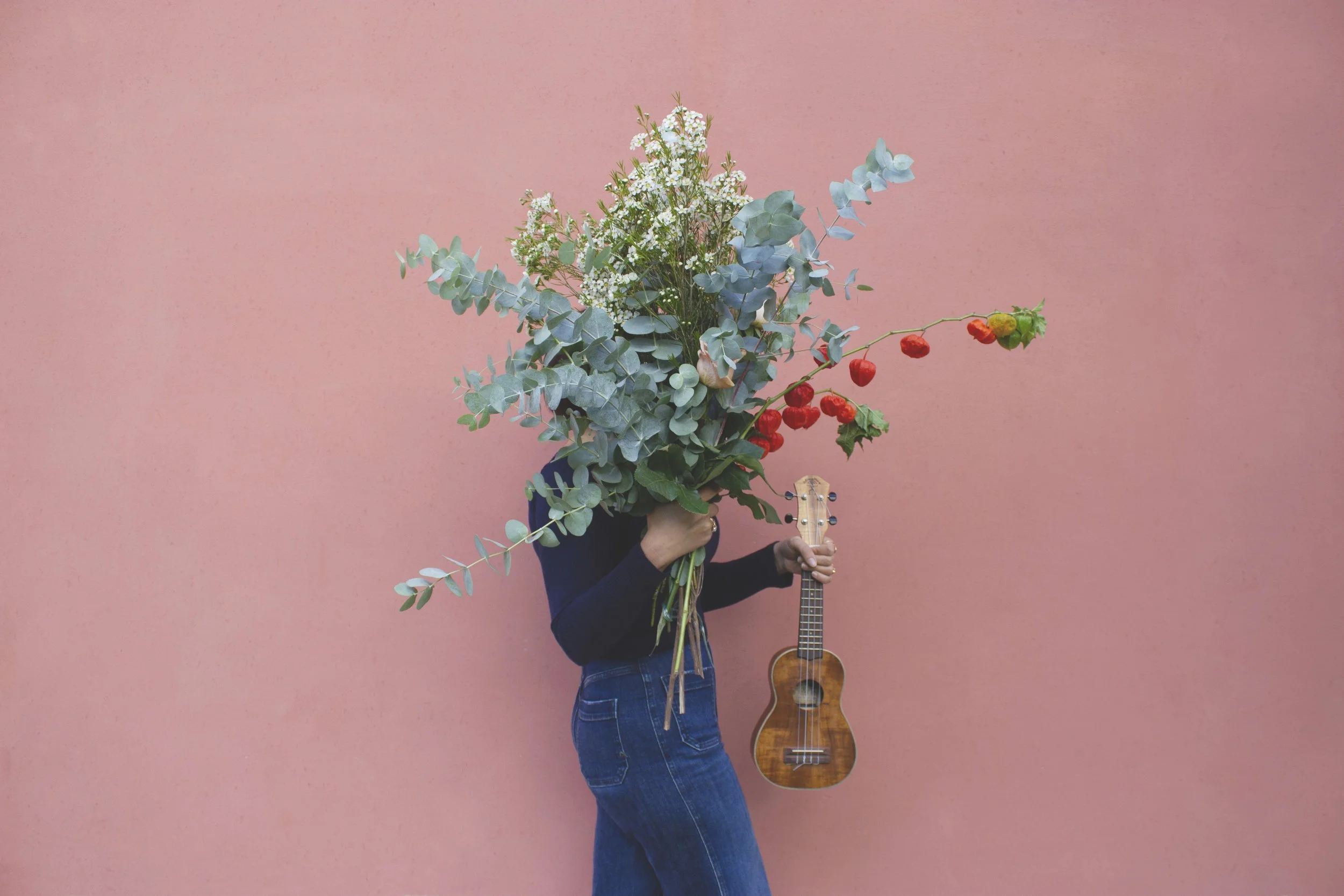 Persona che tiene un mazzo di fiori e uno strumento musicale, una chitarra, con uno sfondo rosa.