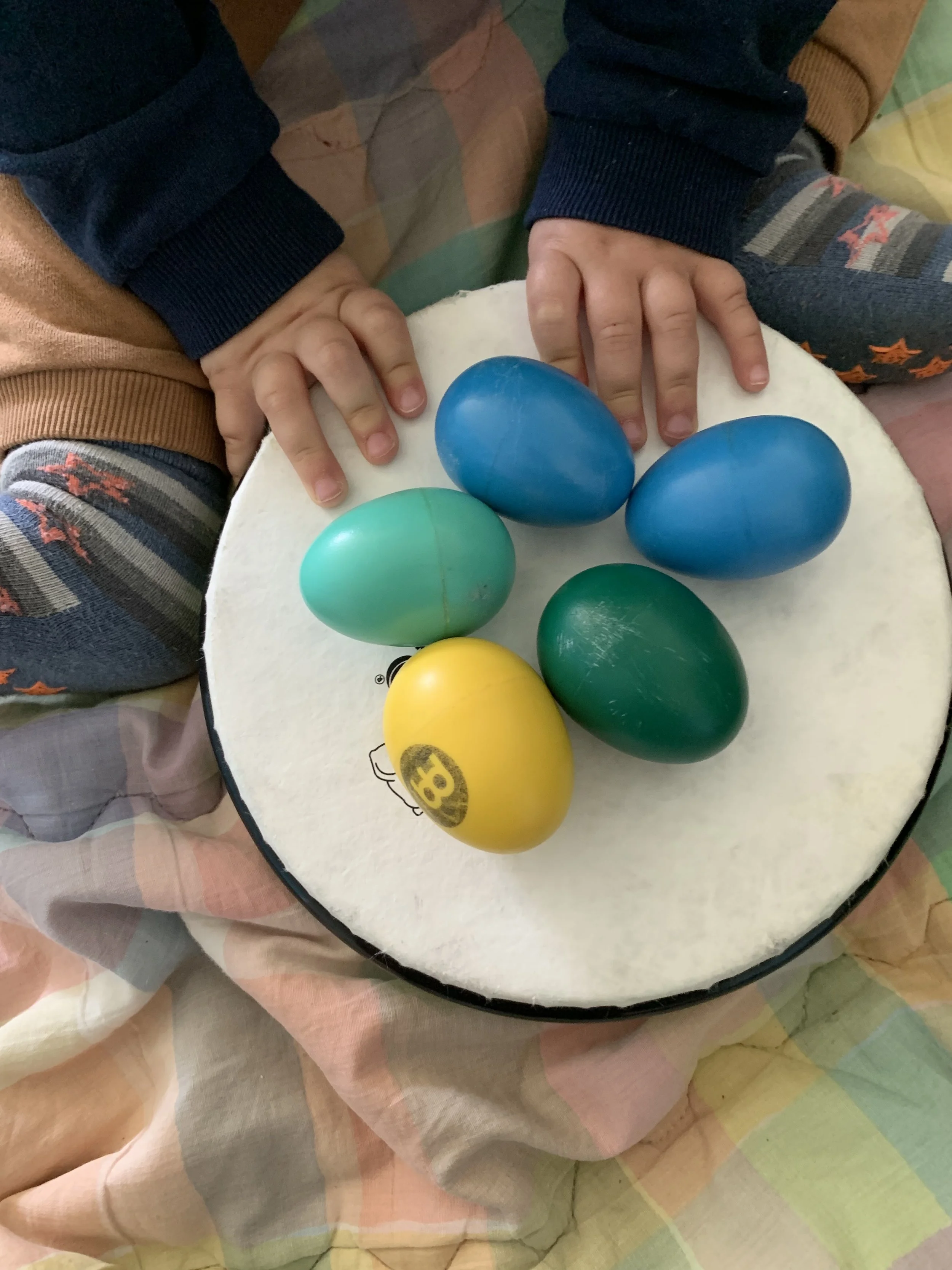 Bambino con maglione a quadri seduto su una superficie con uova di plastica di vari colori