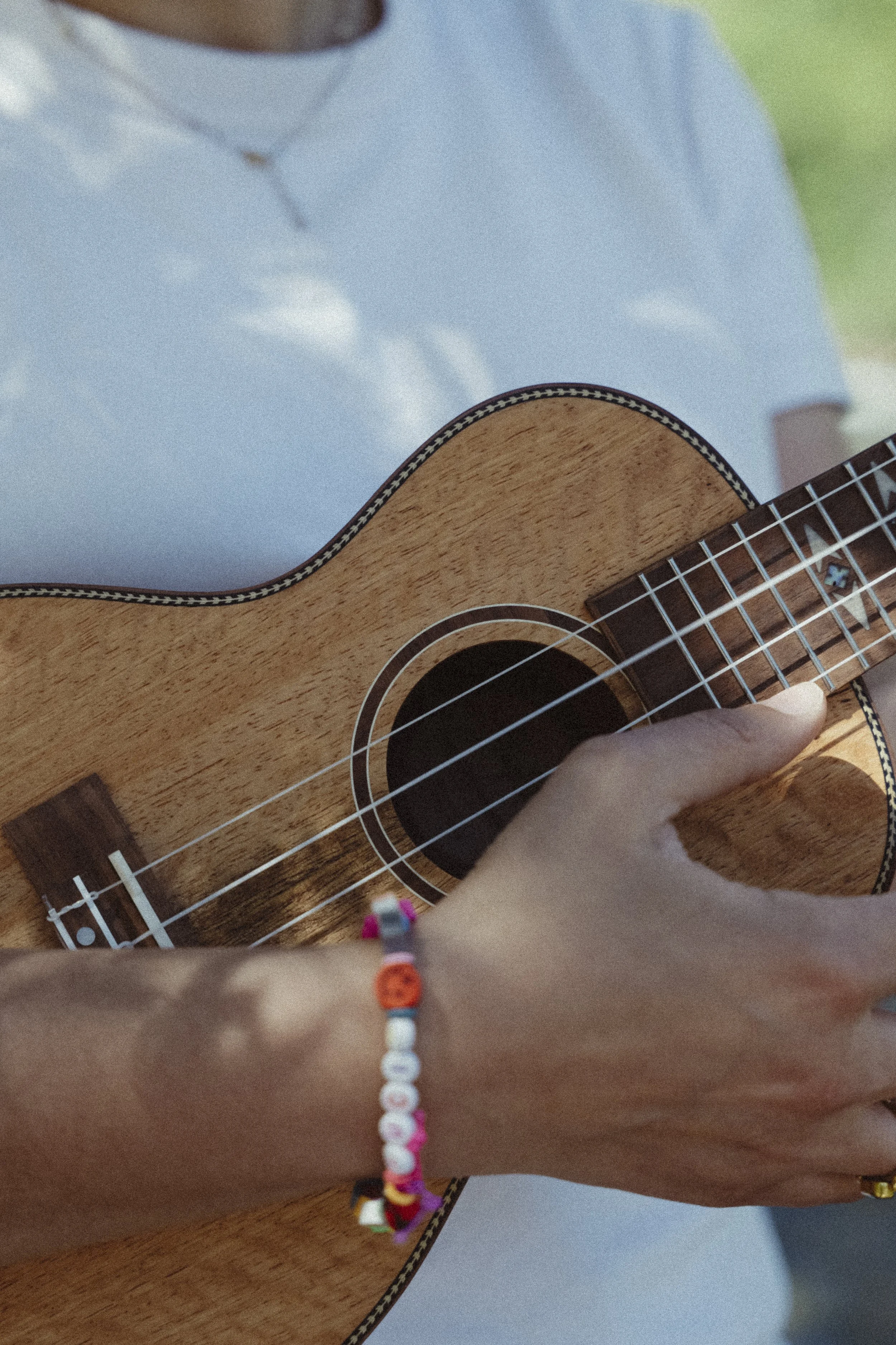 Una mano con un braccialetto di perline colorate regge una chitarra acustica in legno. La persona indossa un vestito beige e il braccialetto mostra diverse perline di vari colori.