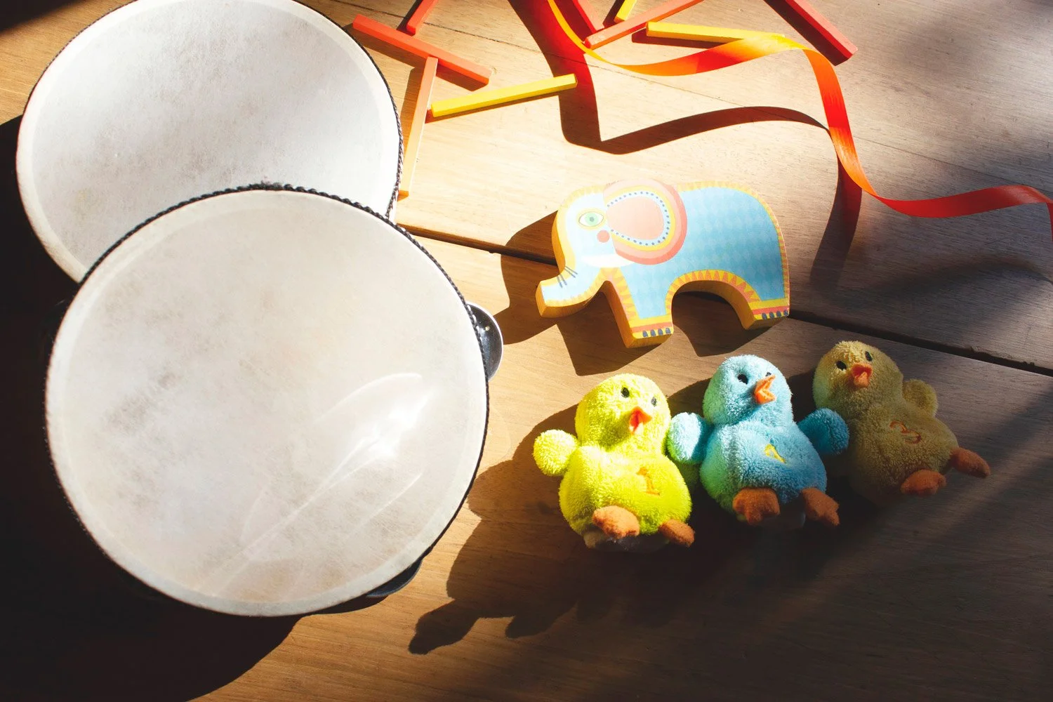 Giocattoli per bambini su un tavolo di legno, tra cui conchiglie, un elefante di legno colorato, uccelli di peluche verdi, blu e gialli e delle bacchette di legno.
