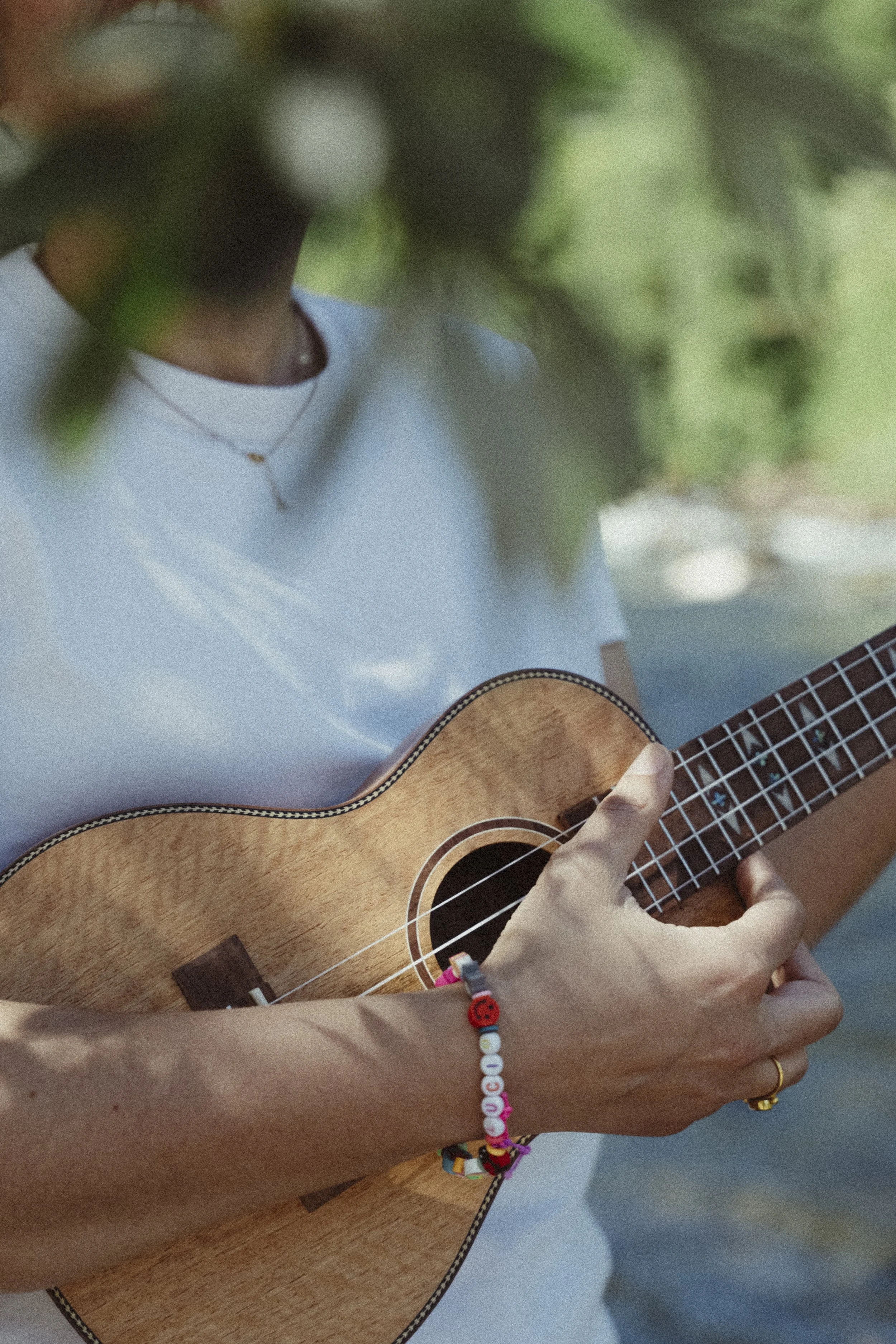 Persona che suona chitarra acustica, vista da sopra, con braccialetti colorati e sfondo verde.