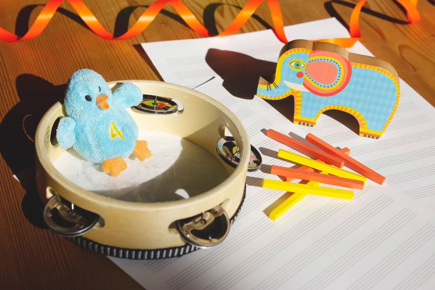 Oggetti colorati per bambini, tra cui un peluche di un uccellino con il numero 4, una scatola di musica, un'elefante di cartone colorato, pezzi di legno colorati, fogli di musica o fogli di carta.
