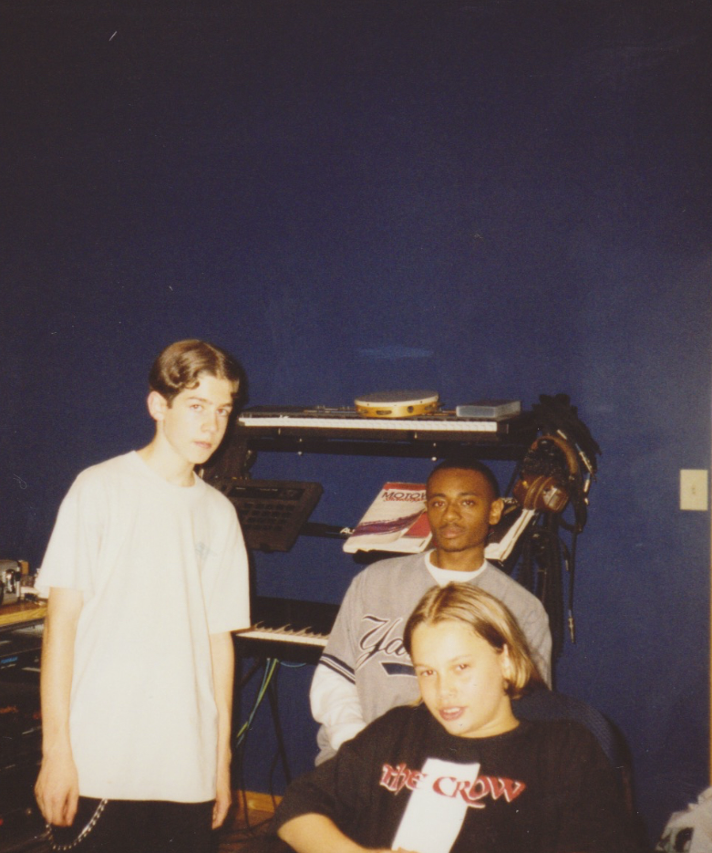 Three young people in a music studio surrounded by musical instruments, including a keyboard and turntables.