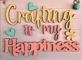 Decorative wall sign with the phrase 'Crafting is my Happiness' in colorful wooden letters, accented with small heart and flower shapes.