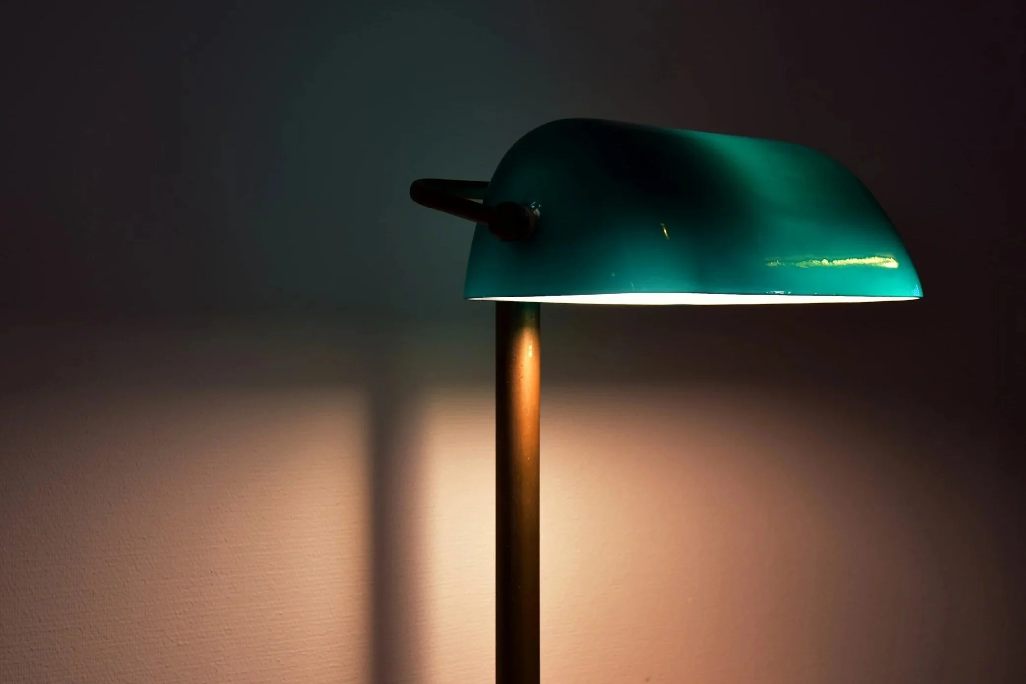 A floor lamp with a teal shade and wooden pole, casting a soft glow on a plain wall.