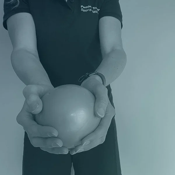 Person in a black polo shirt and black pants holding a medicine ball with both hands.