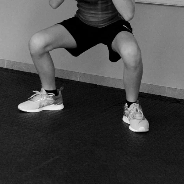 Person performing a squat exercise in a gym, wearing athletic shoes and black shorts.