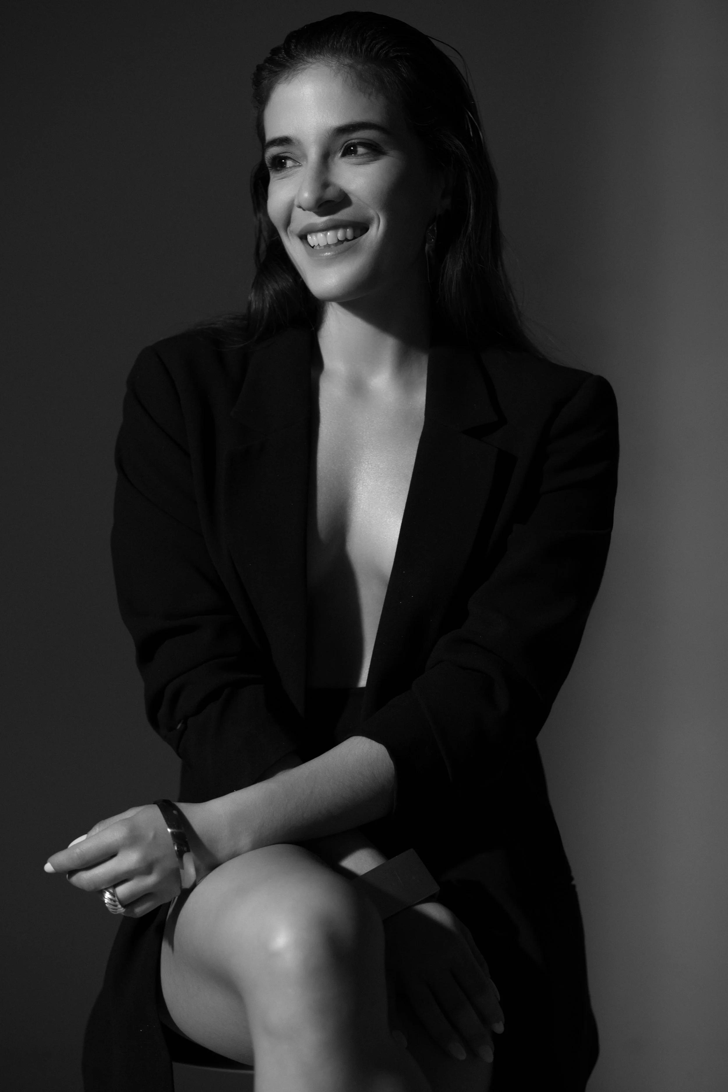 Retrato en blanco y negro de una mujer sonriendo, vestida con blazer negro, cabello suelto, con una actitud relajada y elegante.