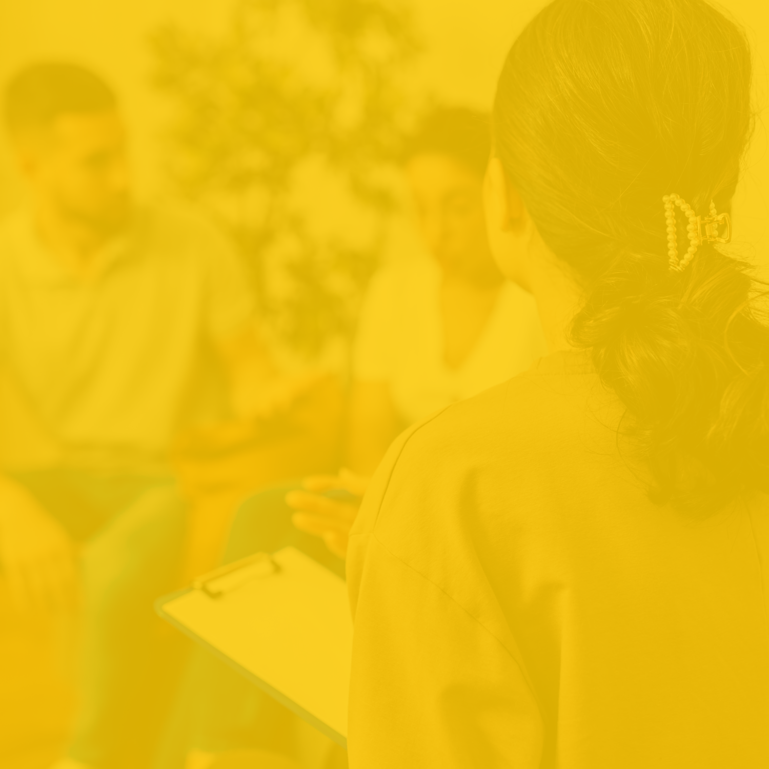 People sitting in a housing counselor's office receiving specialized support ahead of buying their first home. Colorized image with a yellow wash.