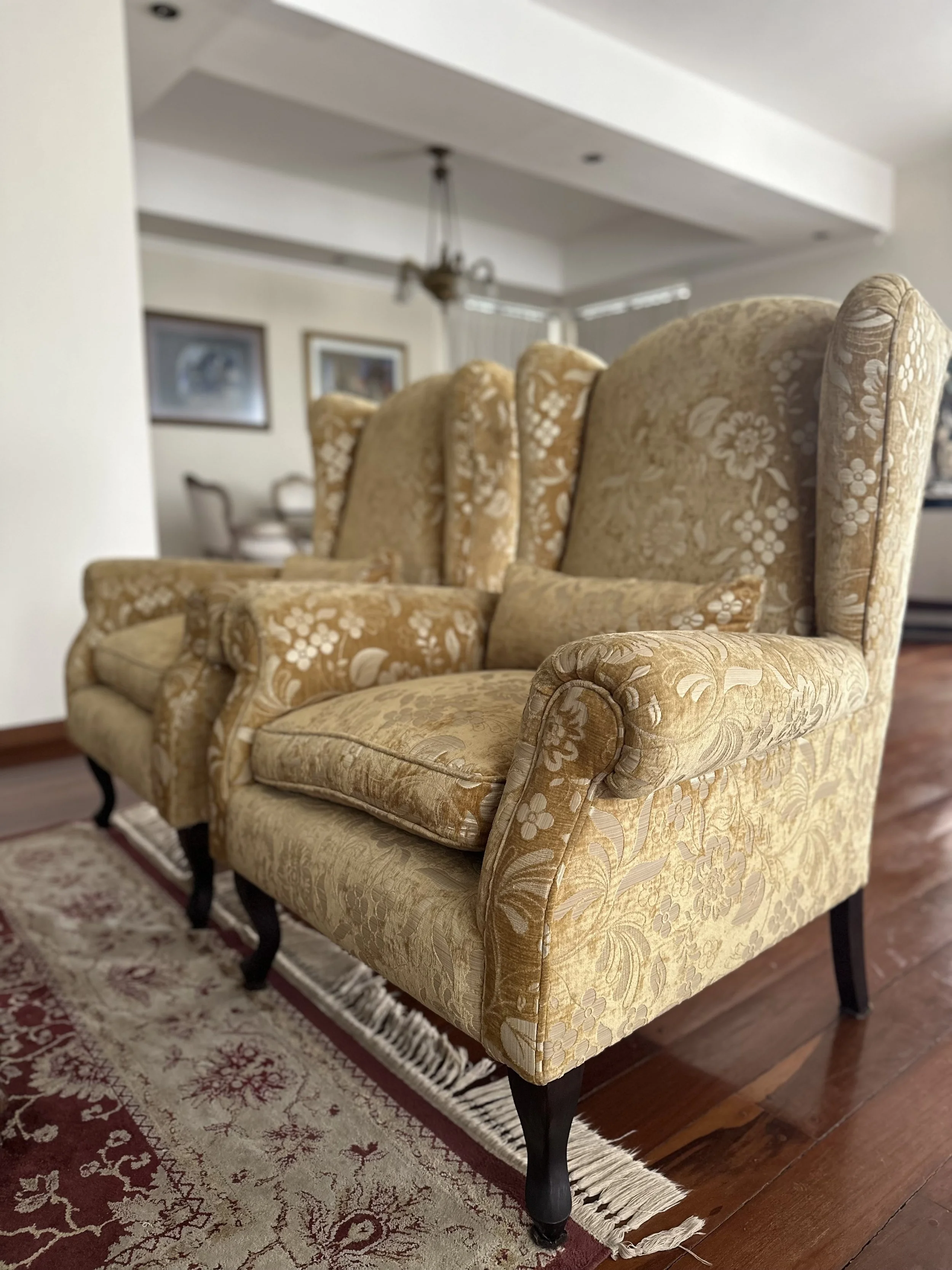 Two vintage armchairs with floral upholstery on a red and beige patterned rug in a living room.
