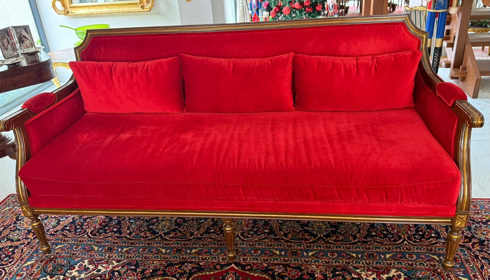 A vintage red velvet sofa with gold detailing in an elegant living room, placed on a patterned rug.