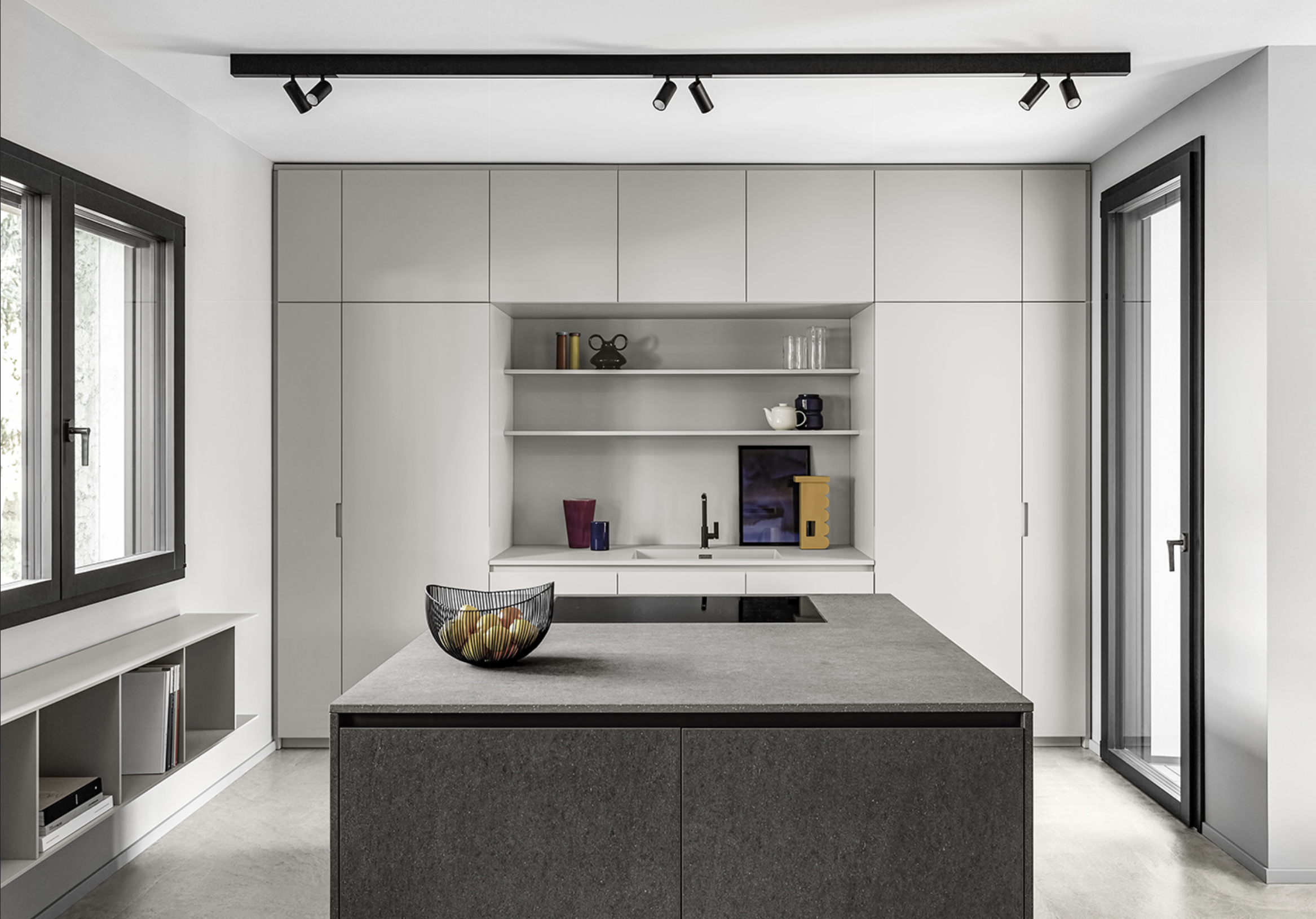 Modern kitchen with white cabinetry, black window frames, a black island with a fruit basket, open shelves with decorative items, and large sliding glass door.
