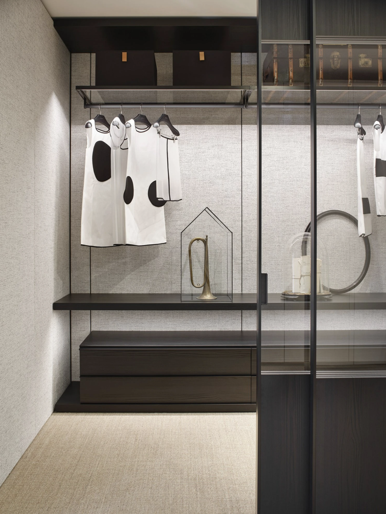 Closet with hanging white clothing with black spots, brass horn under glass display case, and other decorative items on shelves.