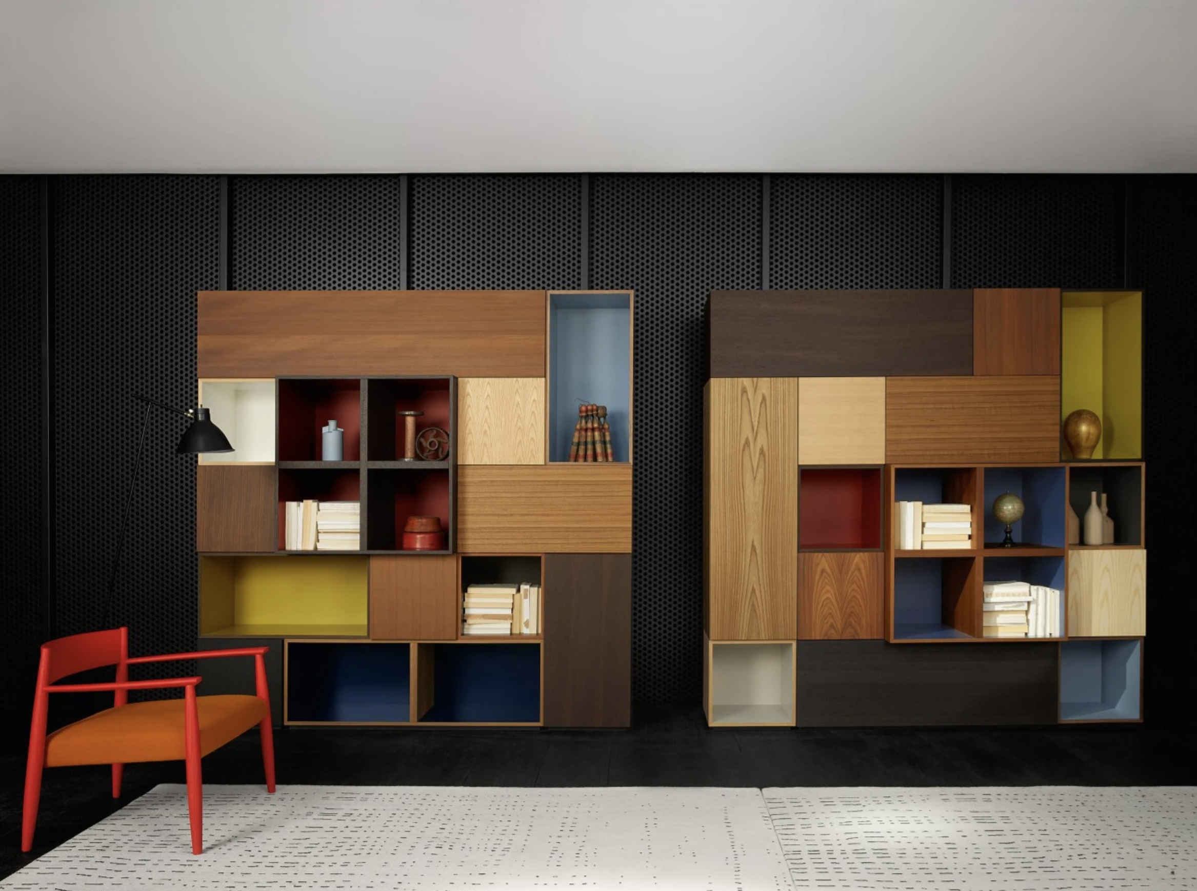 Two modern wooden partition walls with colorful geometric shelving behind them, a black floor lamp, a red chair with an orange cushion, and a white rug with black dots in front of the setup.