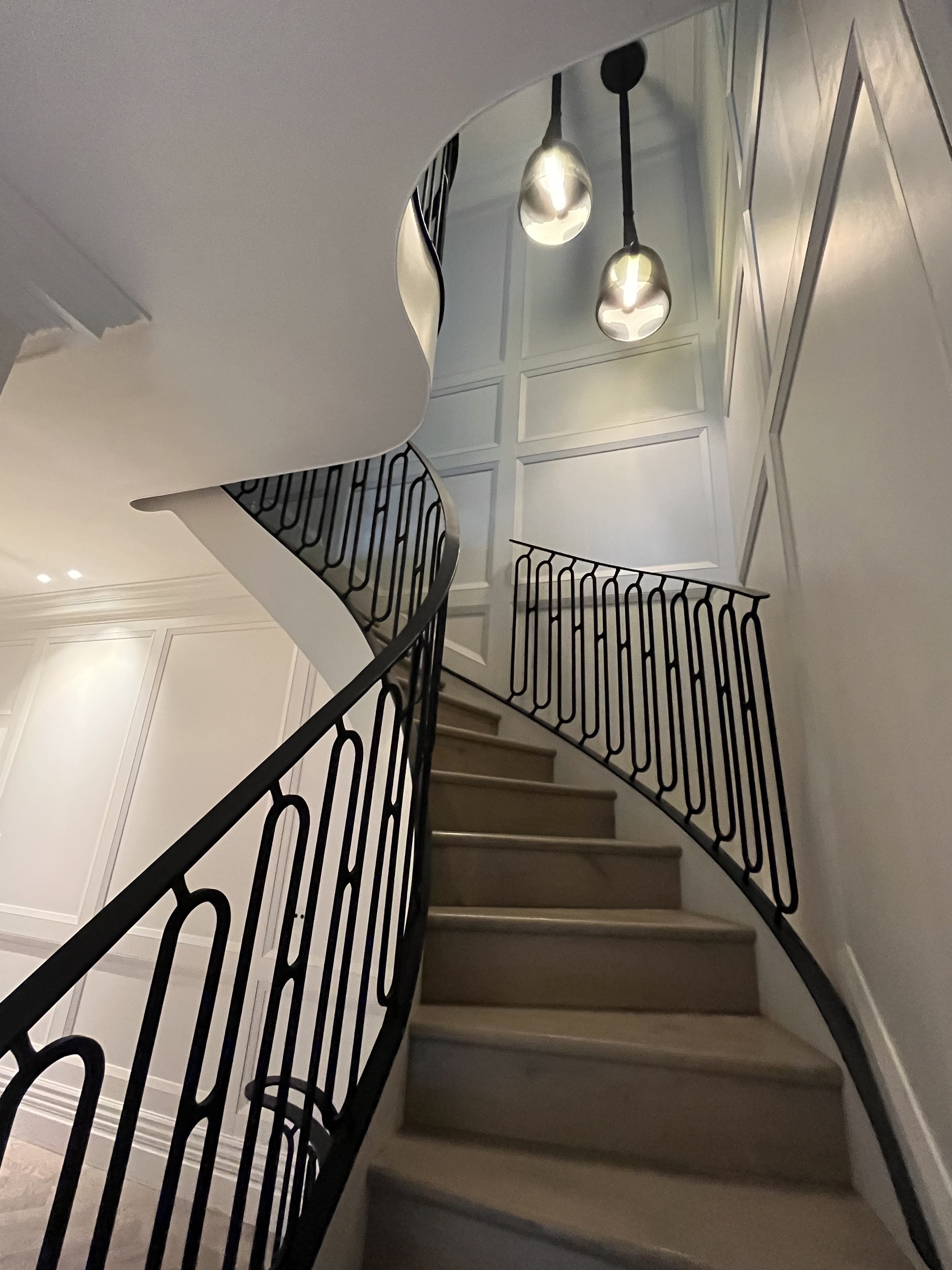 Interior view of a staircase with curved railings, wooden steps, and modern hanging pendant lights in a well-lit home.
