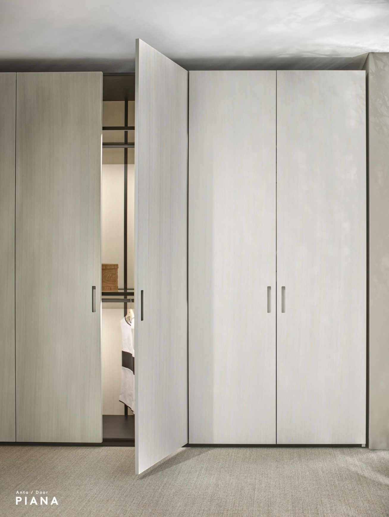 Light-colored sliding wardrobe doors with one door slightly open, revealing a closet with hanging clothes and shelving, in a modern minimalist room.