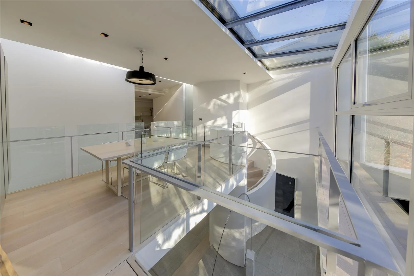 Modern interior space with white walls, a staircase, glass railing, and large windows letting in natural light.