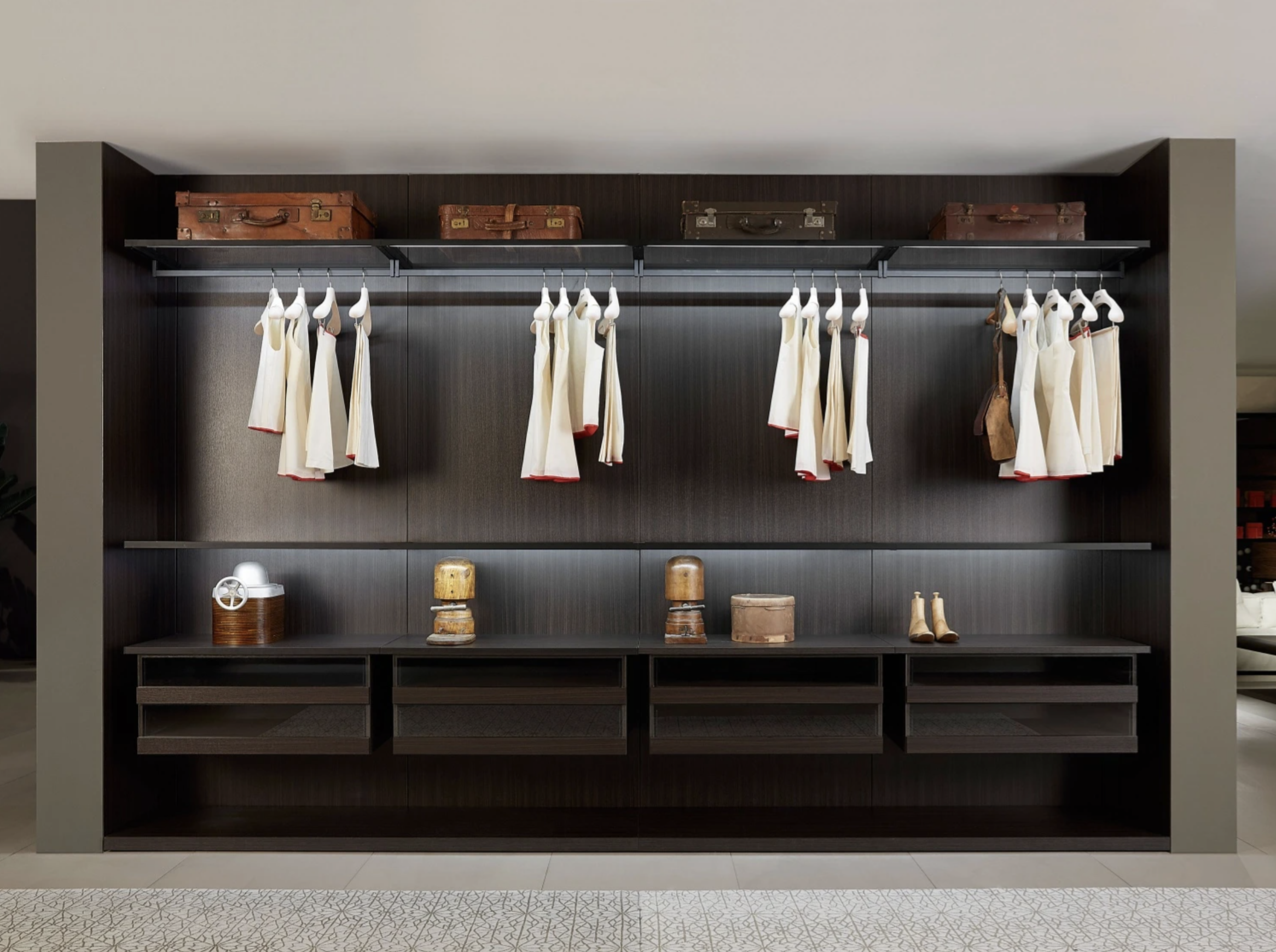 Dark wood closet with hanging white dresses and shelves holding vintage suitcases and accessories.