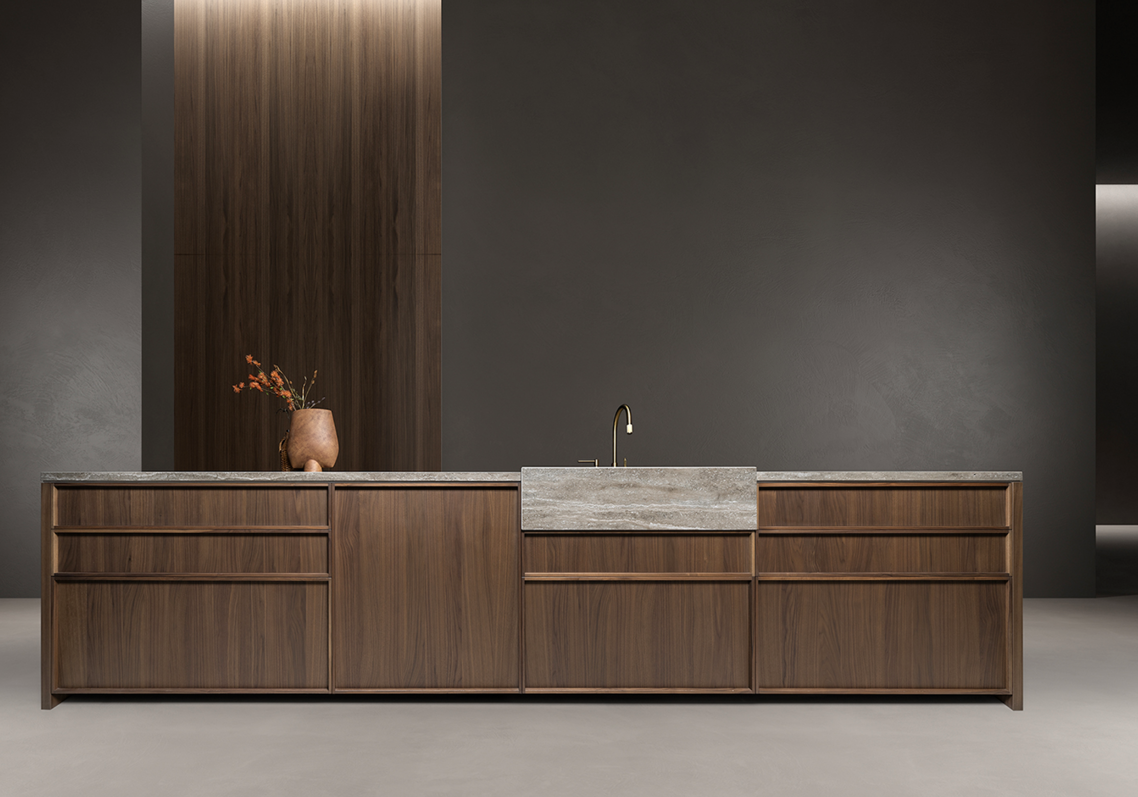 Modern kitchen with wooden cabinetry, dark wall, and a gray stone countertop and sink. A vase with flowers is on the left side of the countertop.