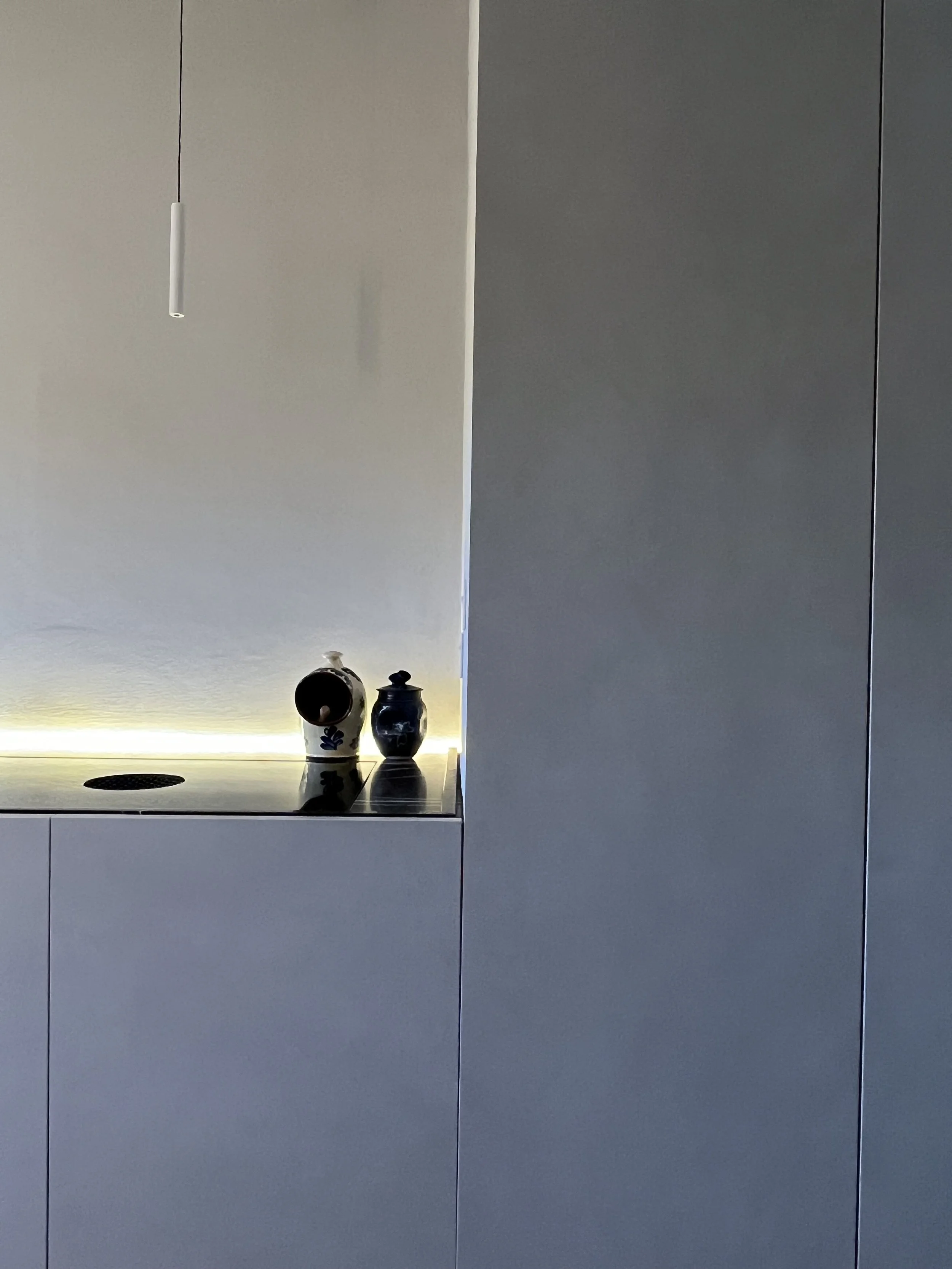 Minimalist interior wall with a ledge holding two decorative vases, one with a black and white pattern and the other solid black, with a modern light fixture hanging above.