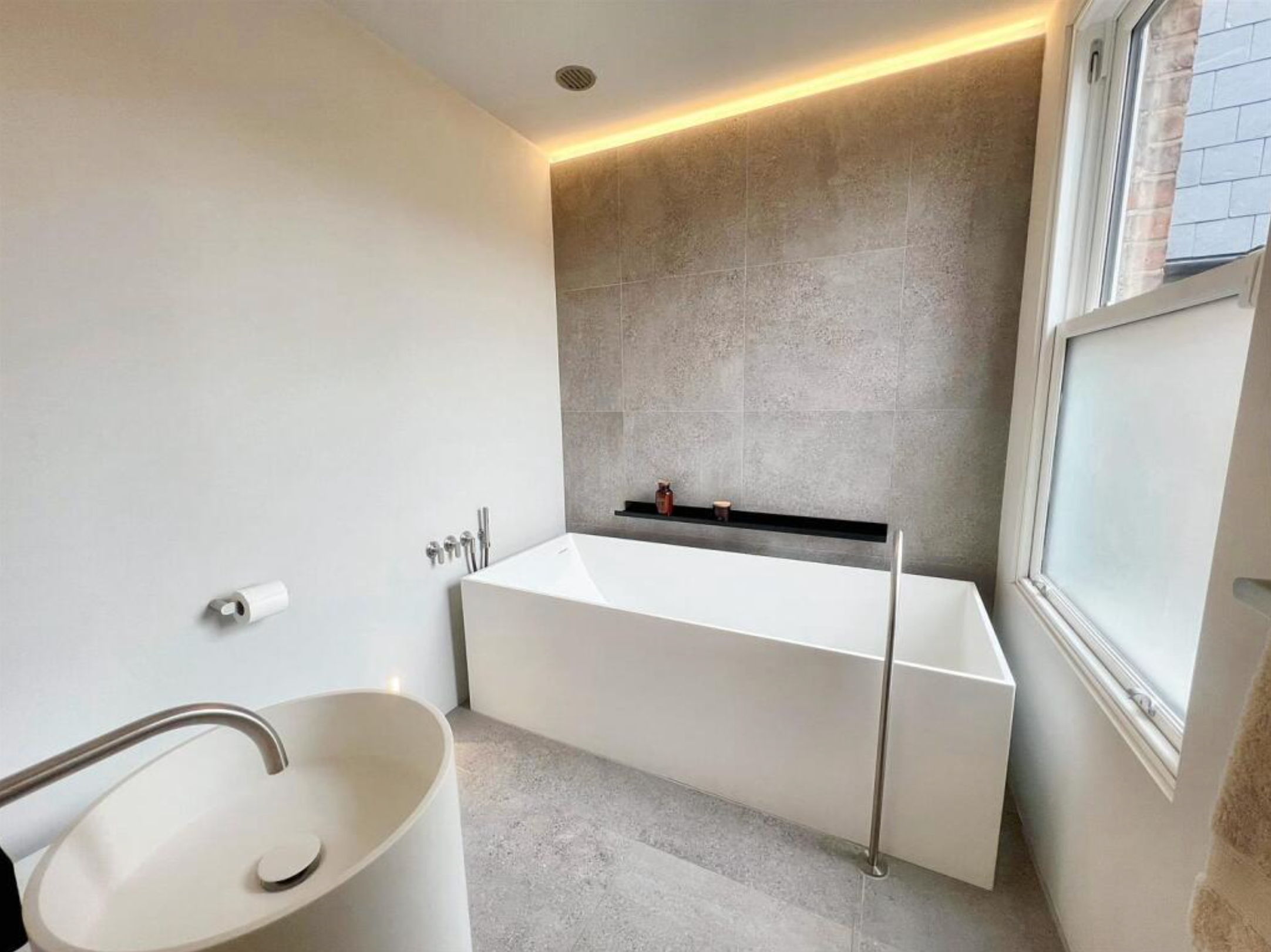 Modern bathroom with a freestanding bathtub, a wall-mounted sink, and a large window.