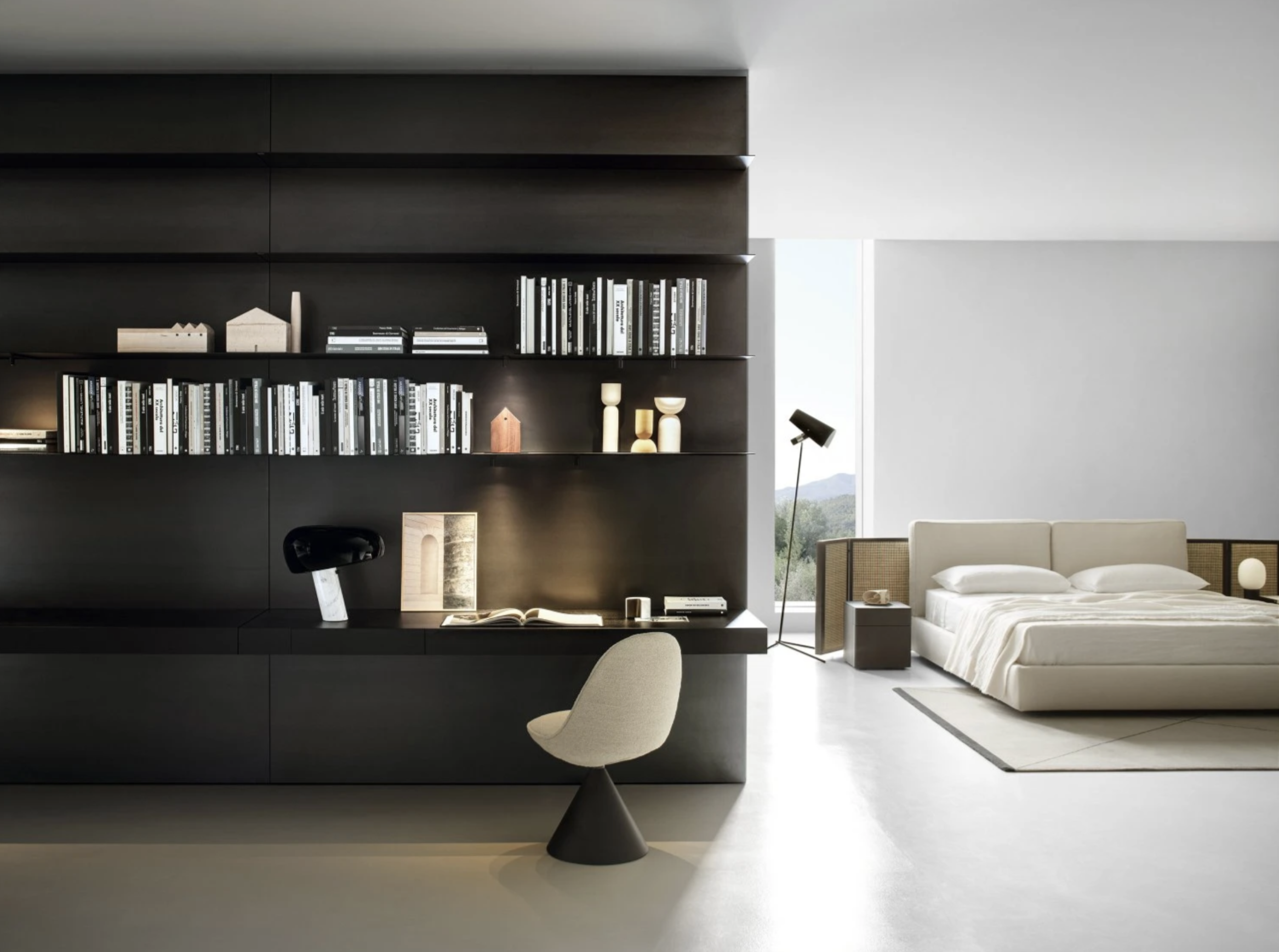 Modern bedroom with black shelving unit, white bed, window with mountain view, black floor lamp, beige chair, and minimal decor.
