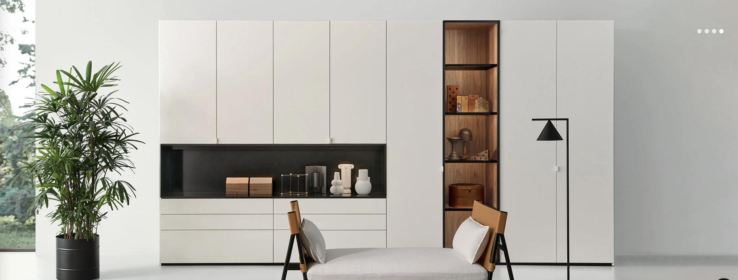 Modern living room with white cabinet wall, large green plant, black and wood accents, white chair with cushion, and decorative items