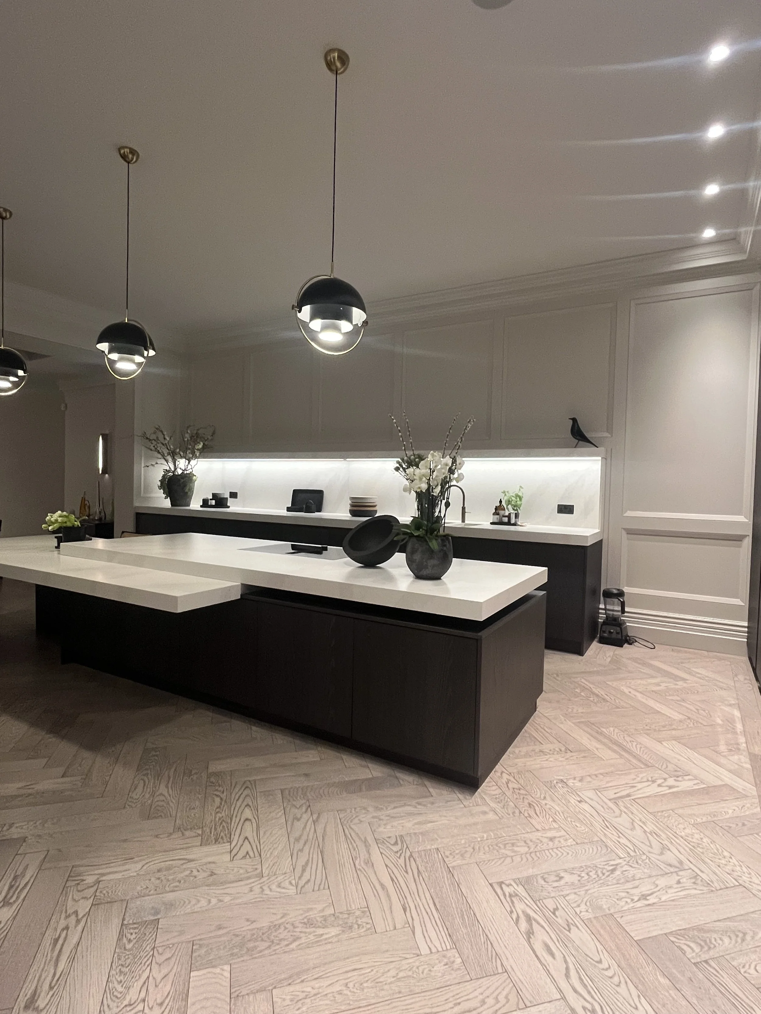 Modern kitchen with black and white color scheme, featuring pendant lights, a large white island with a vase of flowers, and black cabinetry.