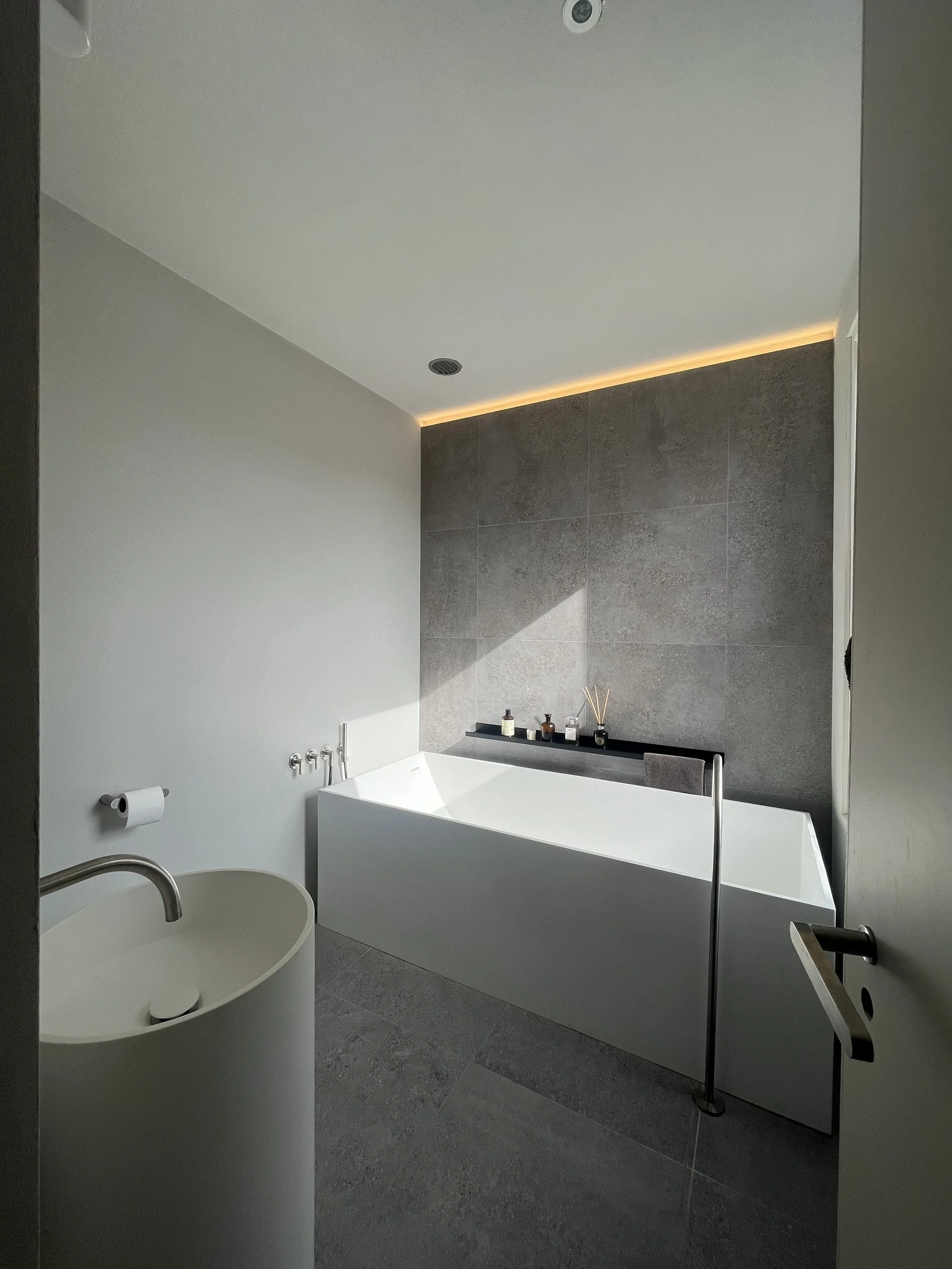 Modern bathroom with a white bathtub, a white oval sink, gray tiles, and minimalist decor.
