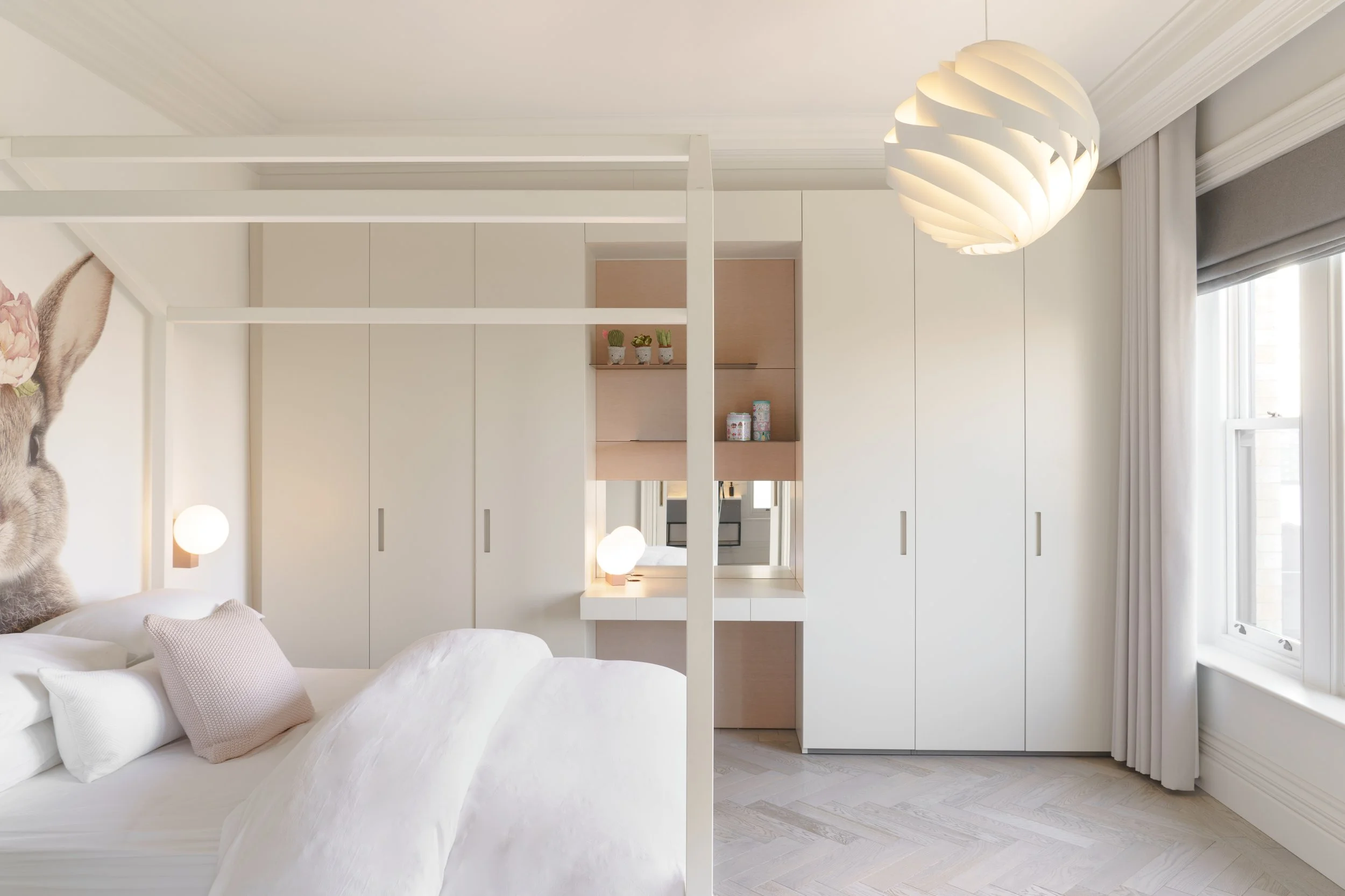 Modern bedroom with a white bed, pink pillow, wall mural of a rabbit with flowers, built-in white wardrobe, mirror and shelves. by Porro and designed by Melides Design, round pendant light, and window with white curtains.