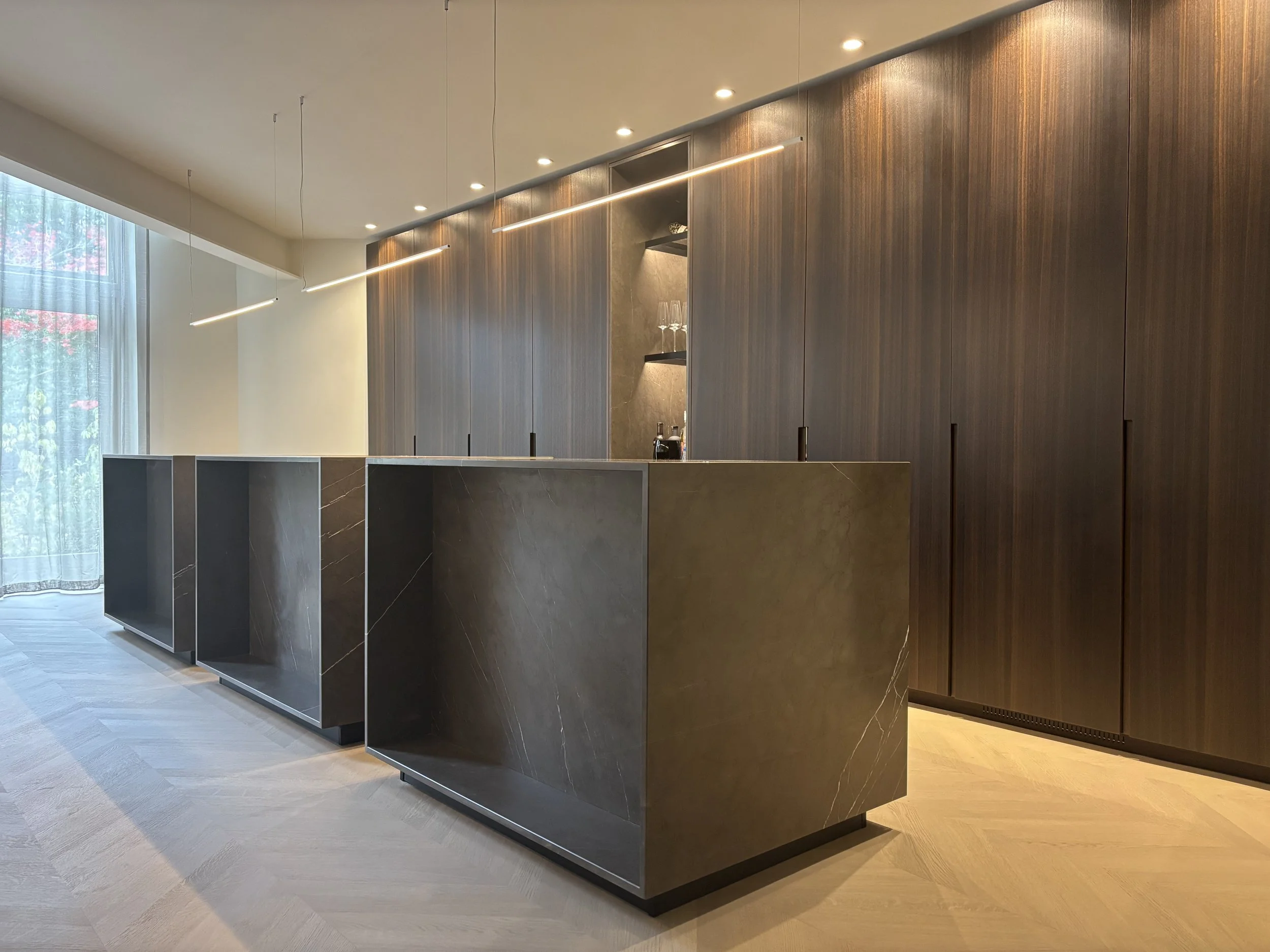 Modern kitchen with a marble island and wooden cabinetry, illuminated by overhead lighting.