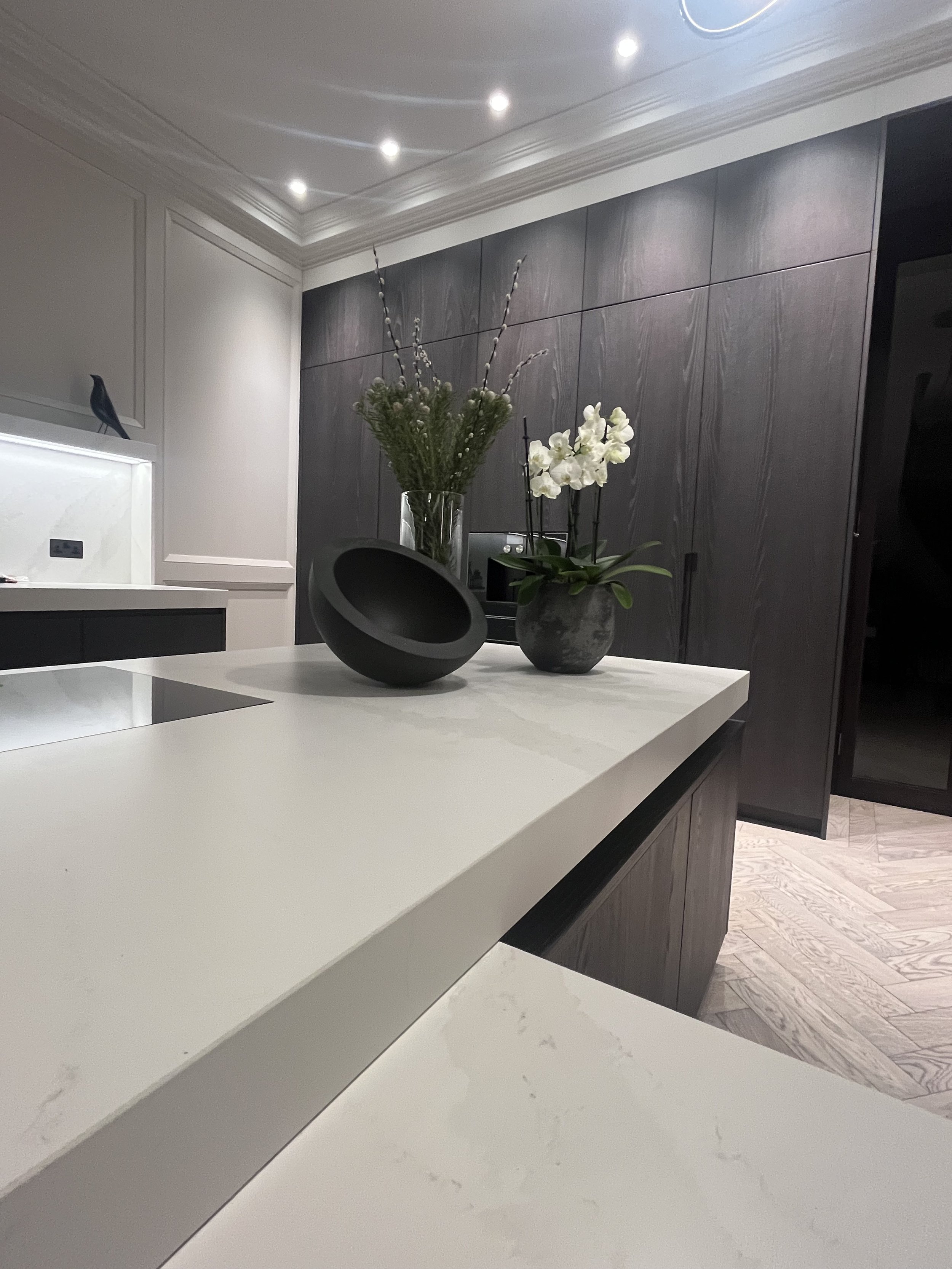 Modern kitchen with Calacatta counter tops and dark stained timber doors designed by Melides Design with a John Pawson bowl,decorative flower vases with white orchids and greenery.
